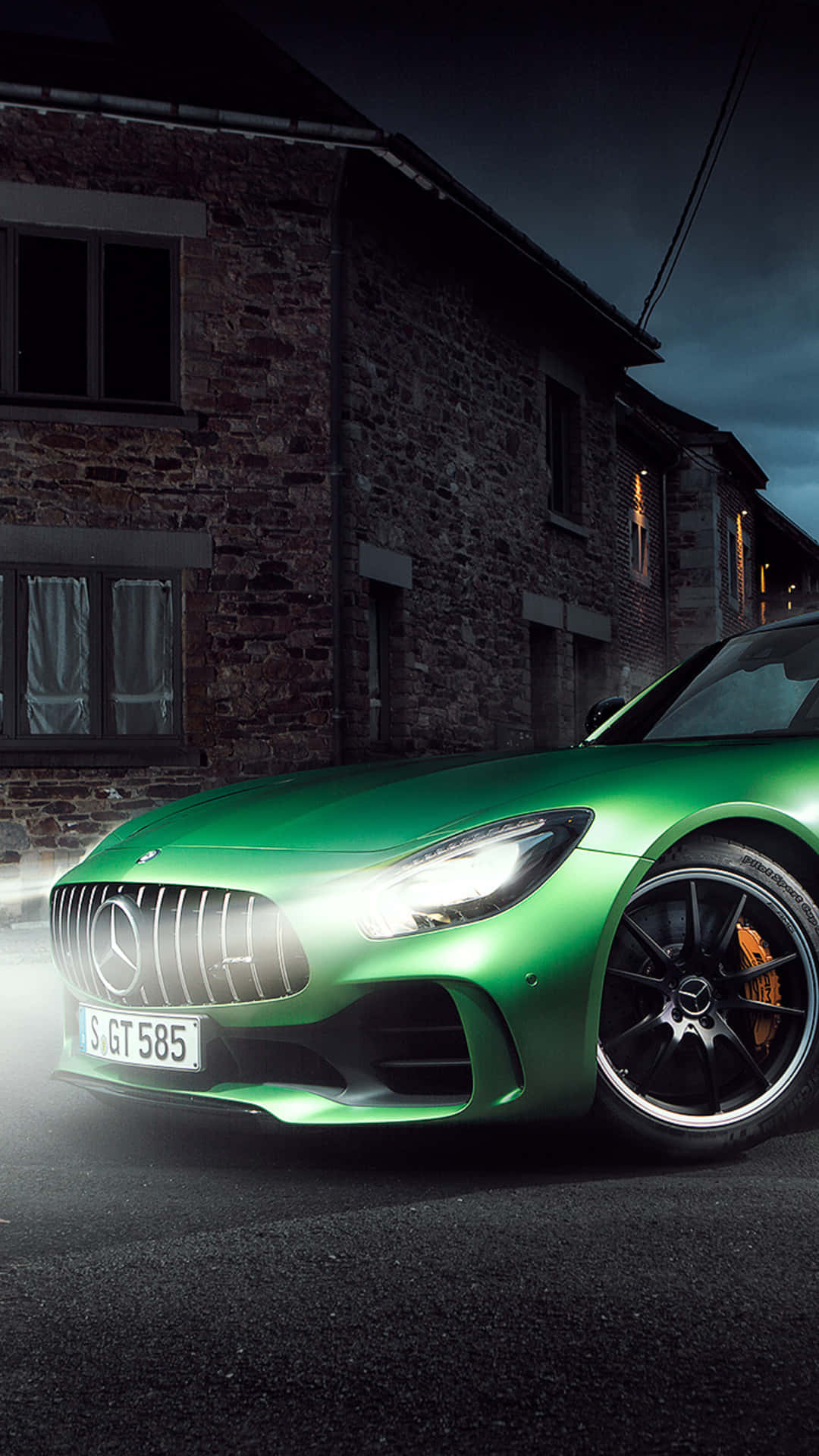 綠色梅賽德斯-AMG GT R 夜間街道背景 壁紙 — 一輛充滿活力的綠色 Mercedes-AMG GT 在夜間停放在一座質樸的石建築前，車頭燈閃閃發光。