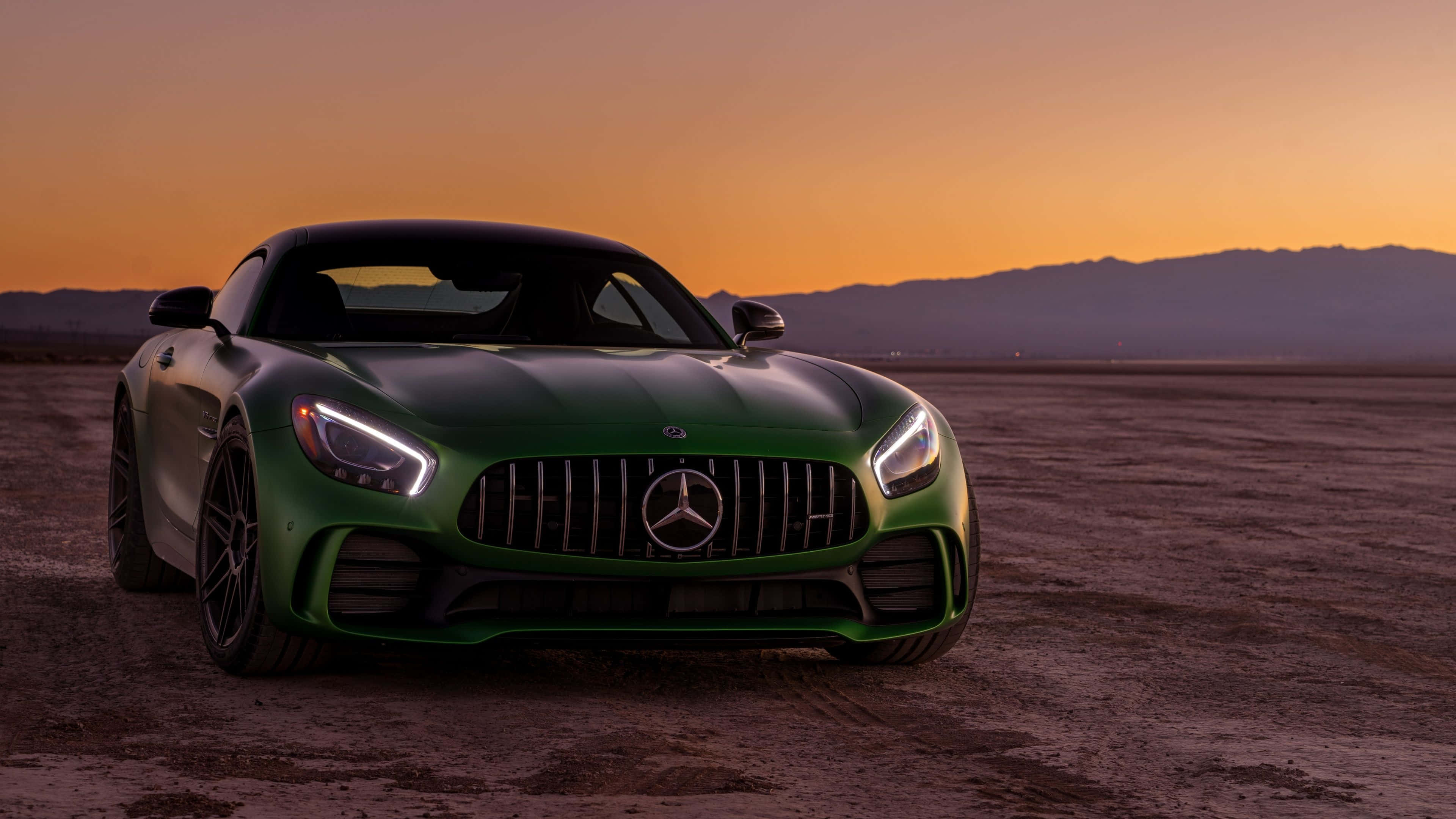 綠色梅賽德斯-AMG GT R搭配夕陽天空背景 壁紙 — 一輛流線型綠色Mercedes-AMG GT跑車在溫暖的日落天空下閃閃發光，背景是遠山。