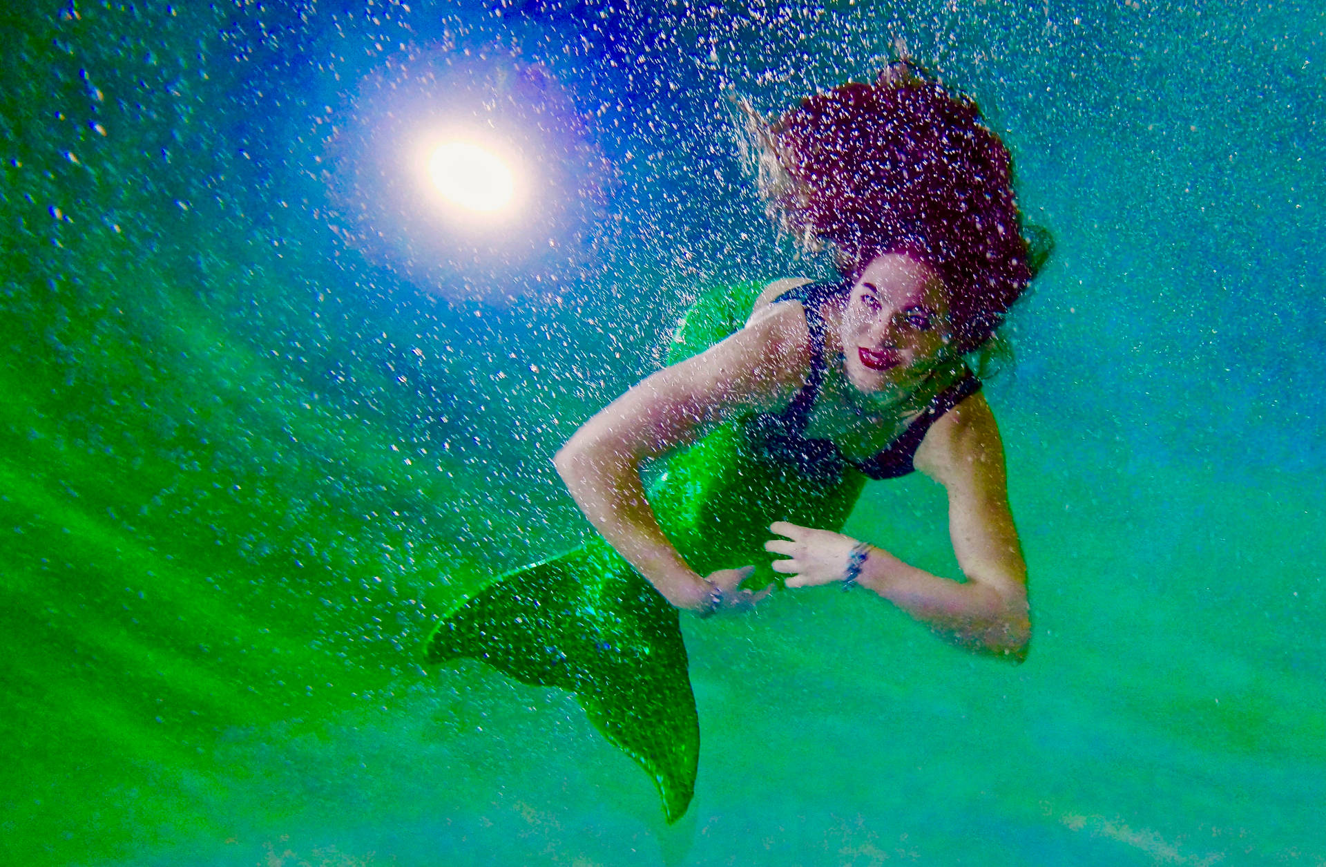 一位紅髮綠尾的美人魚在水下向陽光游去。