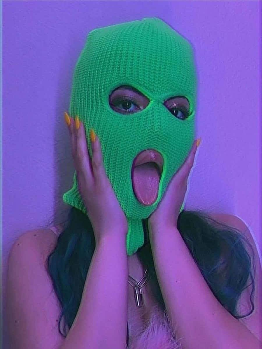 在紫色燈光下，戴著綠色針織面罩，雙手放在臉頰上的人。