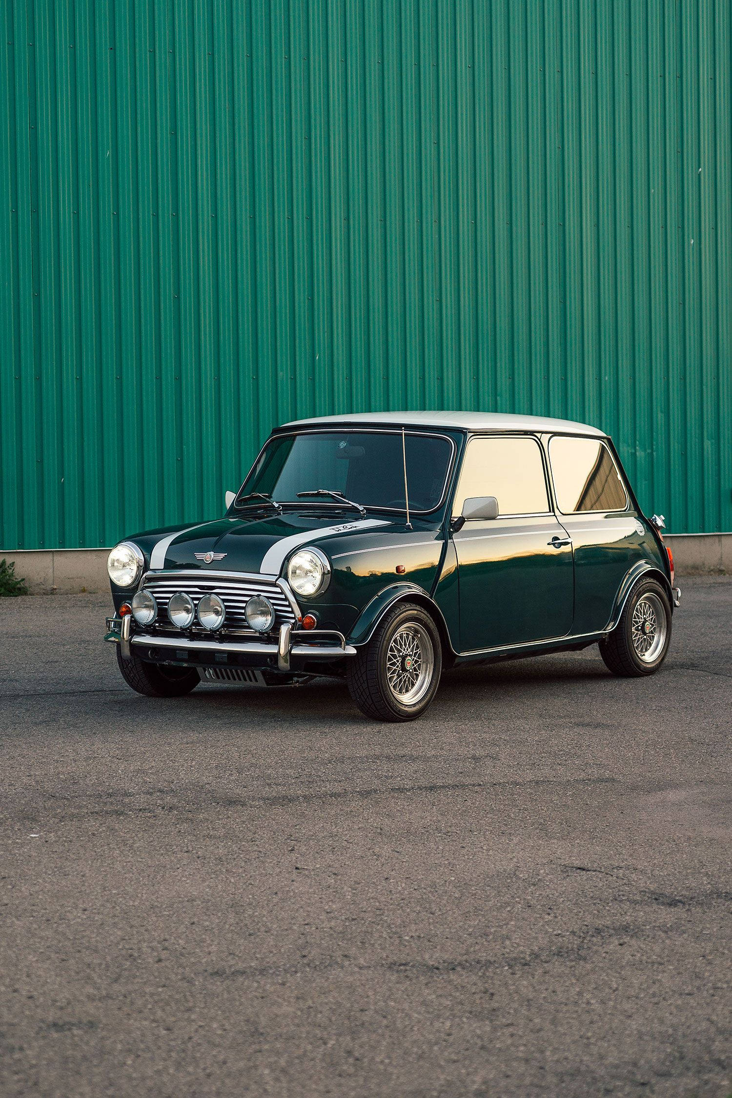 綠色牆前的迷你汽車 壁紙 — 一輛經典綠色MINI Cooper，白色車頂和賽車條紋，停在充滿活力的綠色波紋金屬牆前。