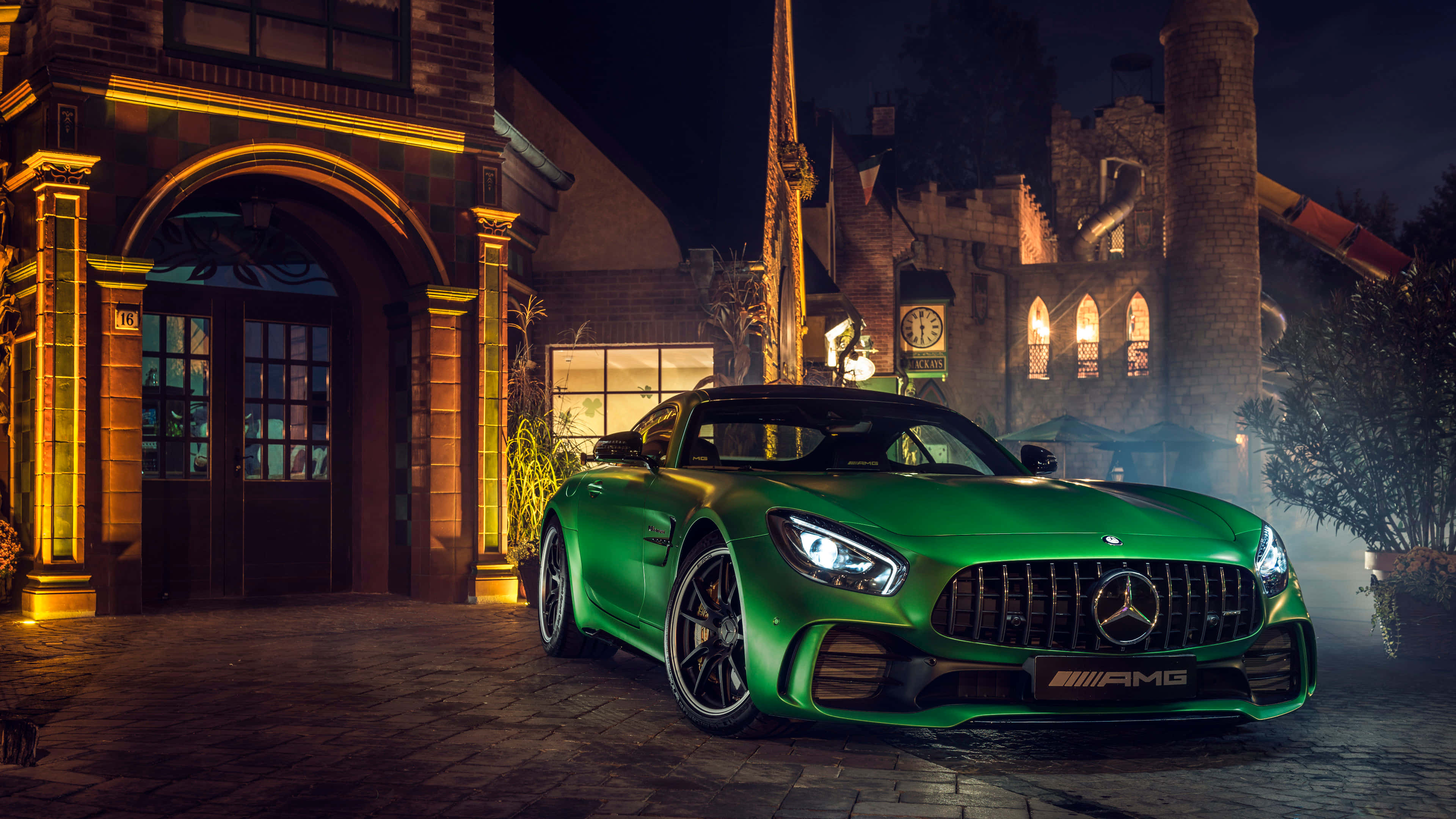 綠色豪華梅賽德斯-奔馳 AMG GT R 車輛背景 壁紙 — 一輛充滿活力的綠色AMG跑車在溫暖的夜燈下閃閃發光，前方是一座哥德式建築，窗戶發光，氣氛迷濛。
