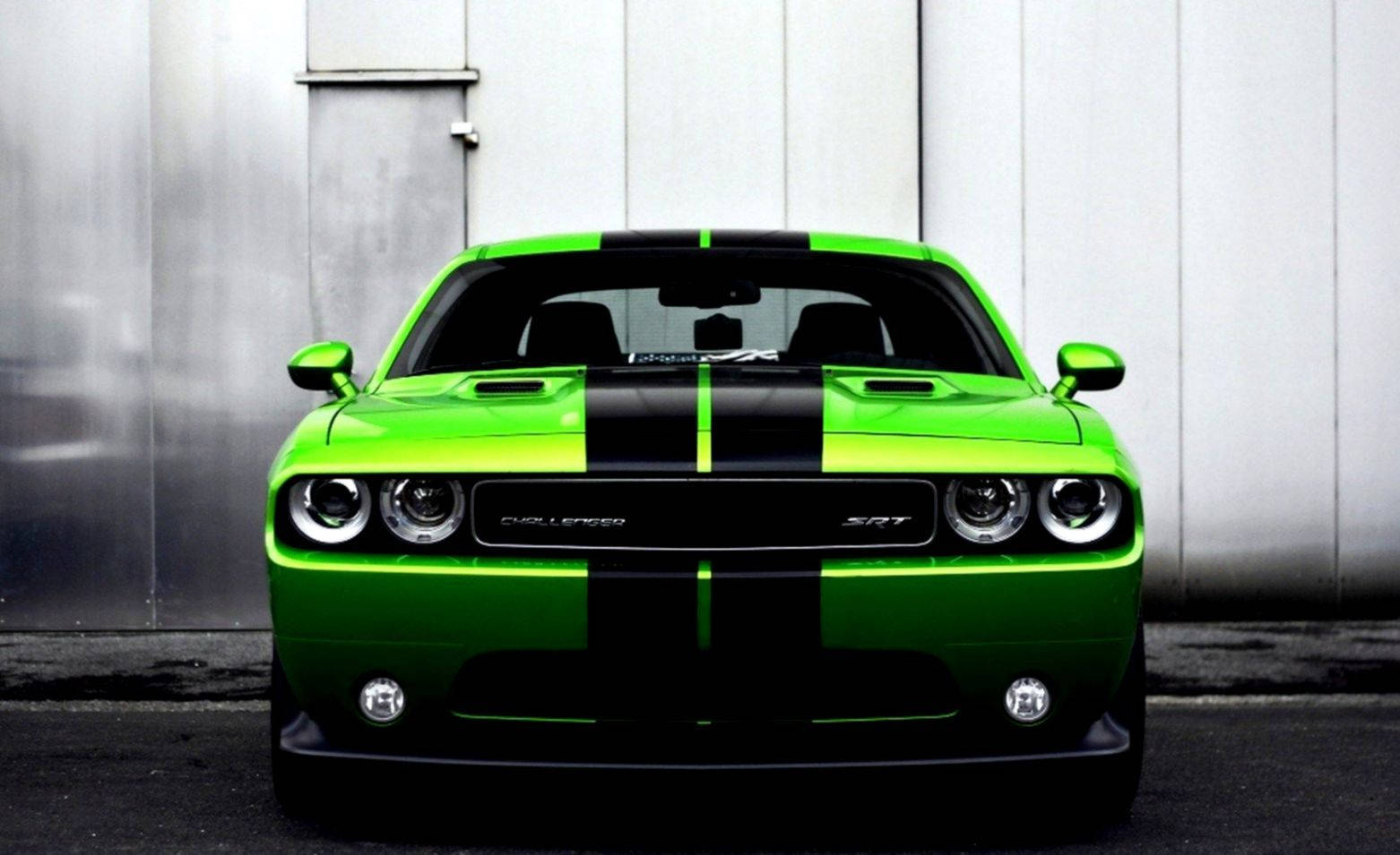 綠色道奇挑戰者 - 力量與風格的典範 壁紙 — 一輛充滿活力的綠色Dodge Challenger SRT，帶有黑色賽車條紋，面向一堵柔和的工業牆。