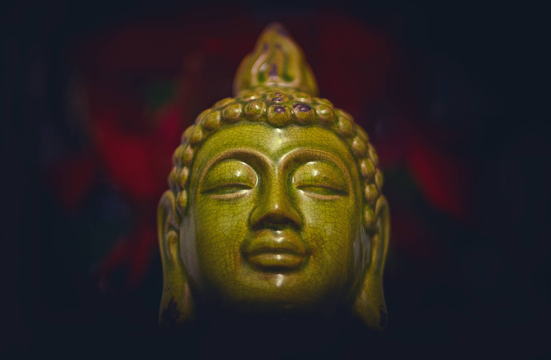 特寫一個綠色佛像頭像，閉著眼睛，帶有裂紋釉面。