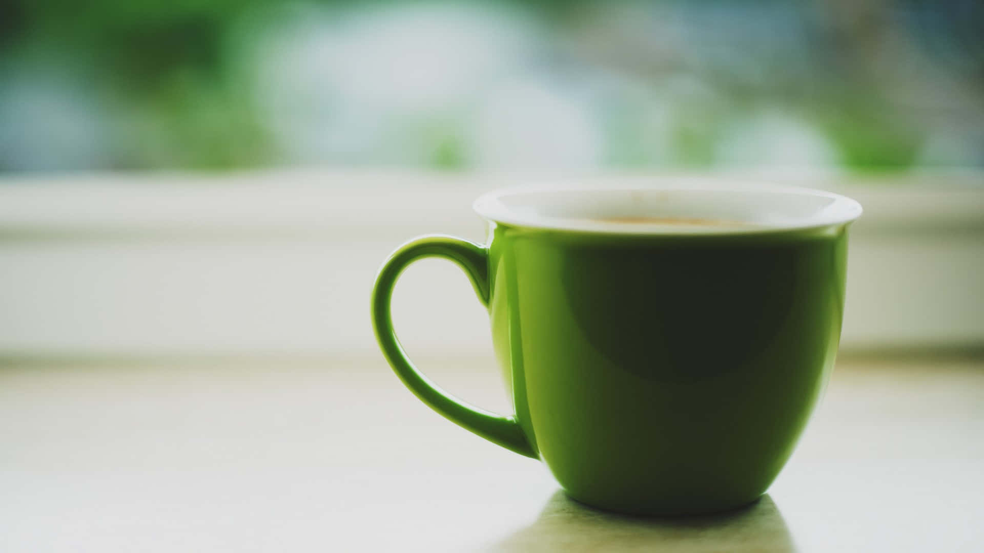 綠茶杯圖 壁紙 — 一個充滿活力的綠色陶瓷杯，裝滿冒著蒸汽的咖啡，放在灑滿柔和自然光的窗台上。
