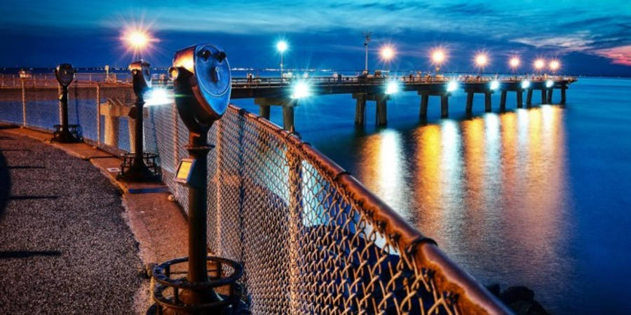 維吉尼亞海灘碼頭夜景 壁紙 — 黃昏海濱場景，亮著的投幣式望遠鏡俯瞰著延伸至平靜水面的發光碼頭。