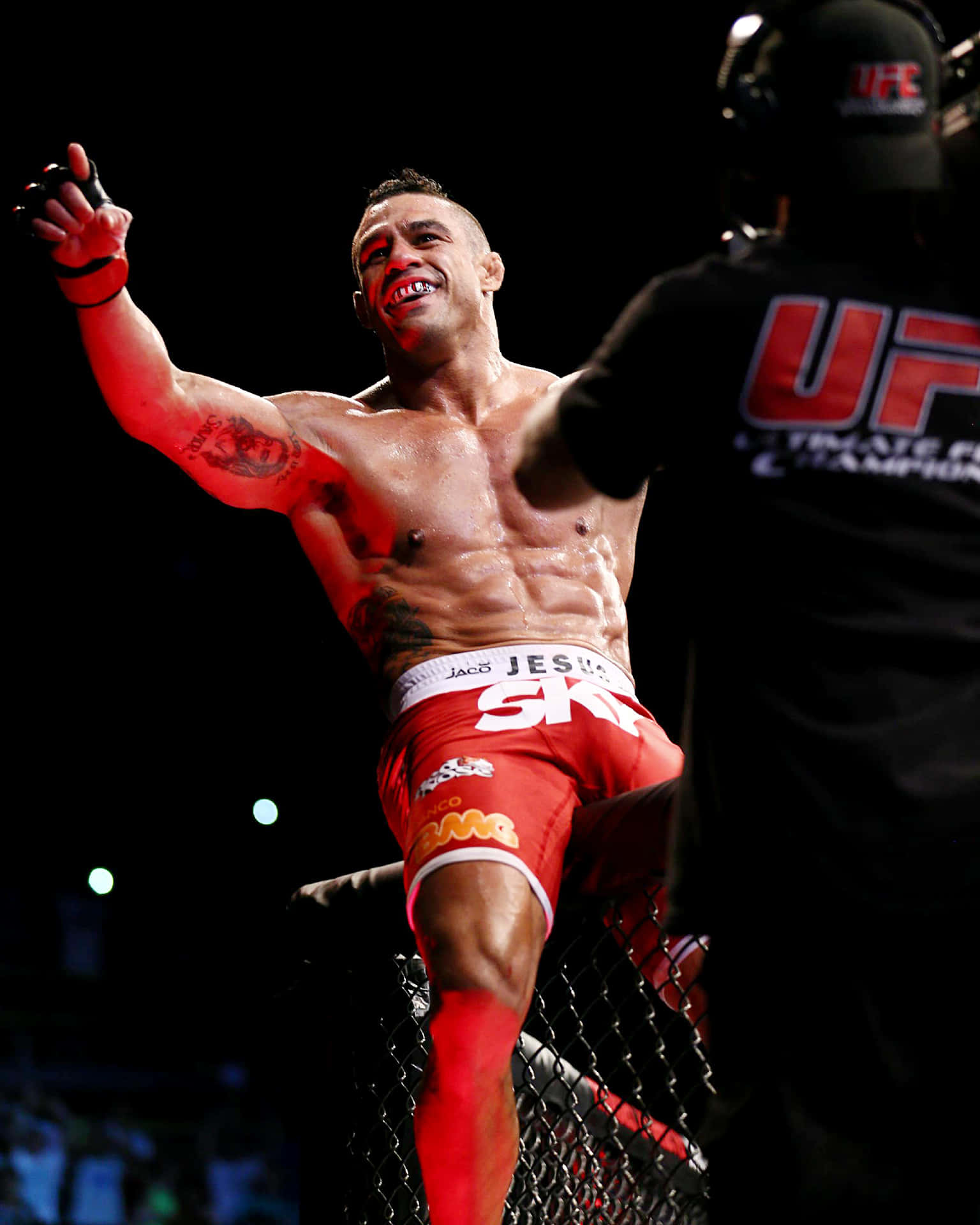 維托·貝爾福特在2013年UFC on FX 7賽事中的勝利瞬間 壁紙 — 一位身穿紅色短褲的勝利UFC拳手在明亮的競技場燈光下，於八角籠內舉起拳頭慶祝。