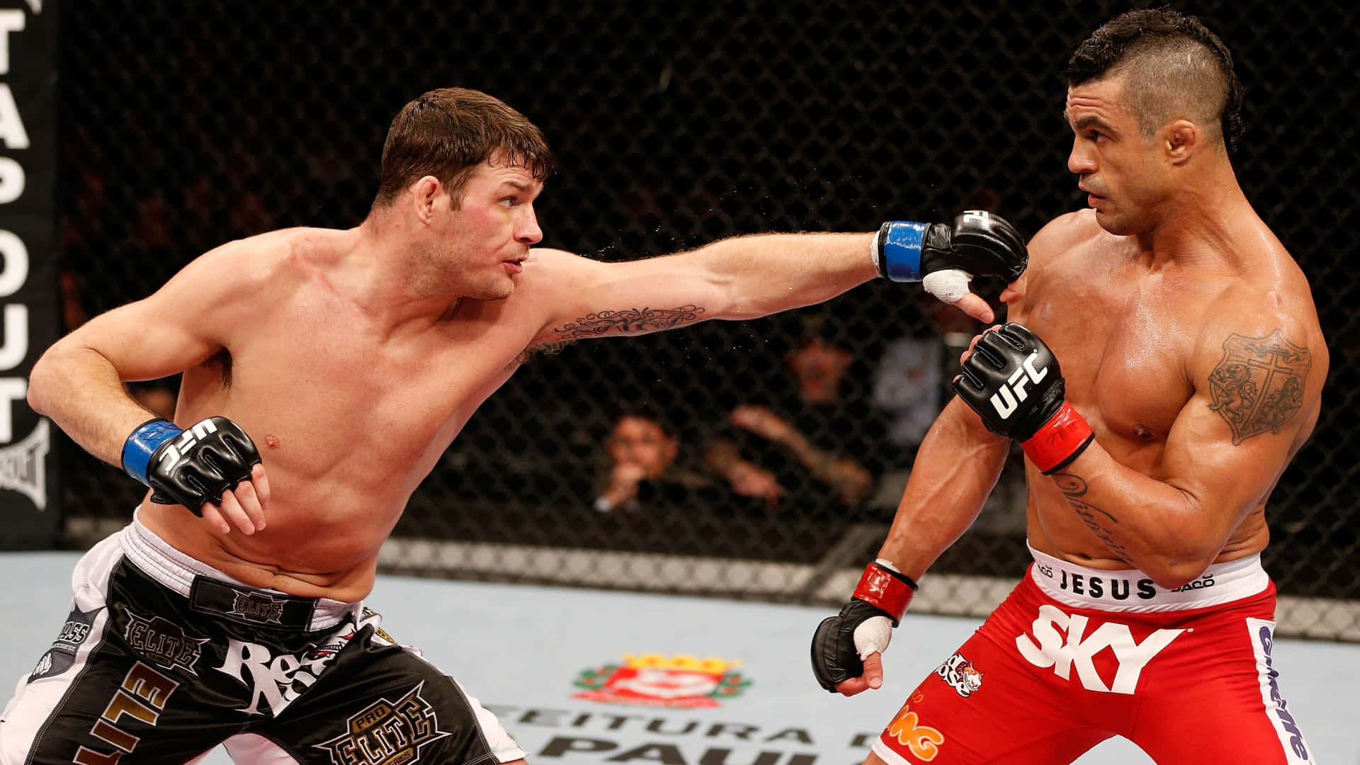 維托·貝爾福特對戰麥克·比斯平 UFC On FX 壁紙 — 兩名肌肉發達的MMA拳手在激烈的籠鬥中交鋒，汗水飛濺，其中一人打出強力一拳。