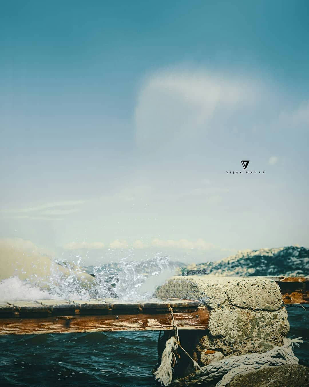 海浪拍打著一條木碼頭，有石柱和繩索，天空湛藍。