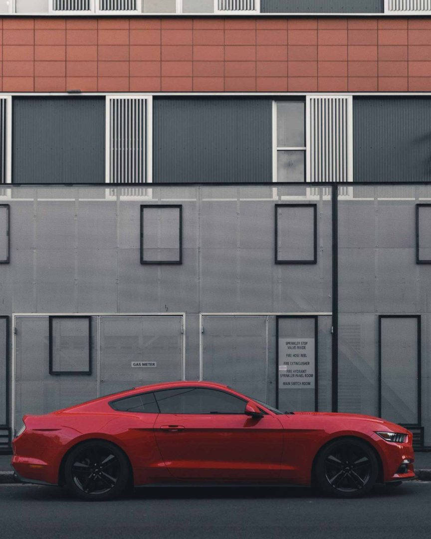 紅色跑車停在一棟灰色和橙色建築旁。
