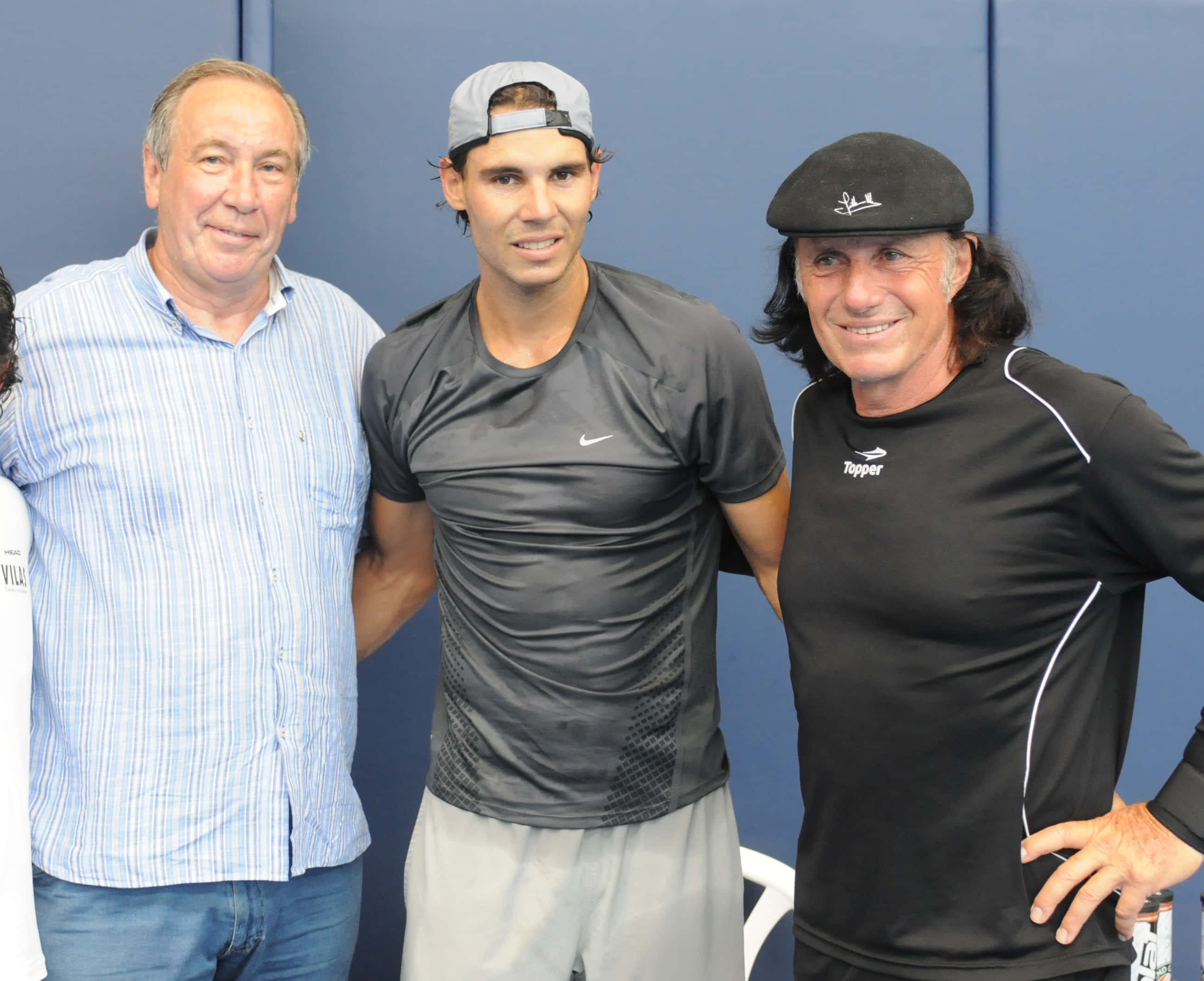 網球巨星古鐵雷斯·維拉斯與納達爾與粉絲同框 壁紙 — 三個男人一齊喺純藍色牆前面擺甫士，一個著運動裝，另一個著間條衫，第三個戴黑色帽同著黑色衫。