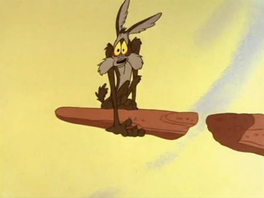 綿羊犬威爾·E·科伊ote站在斷崖邊 壁紙 — Wile E. Coyote 企喺浮石上，面對溫暖嘅黃色天空，表情驚嚇。