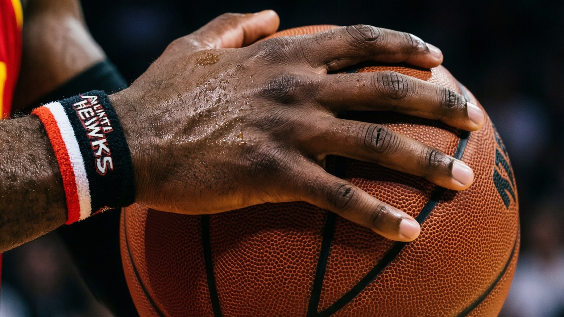 汗流浹背的籃球運動員的手緊握著一個帶有Hawks腕帶的橙色球。