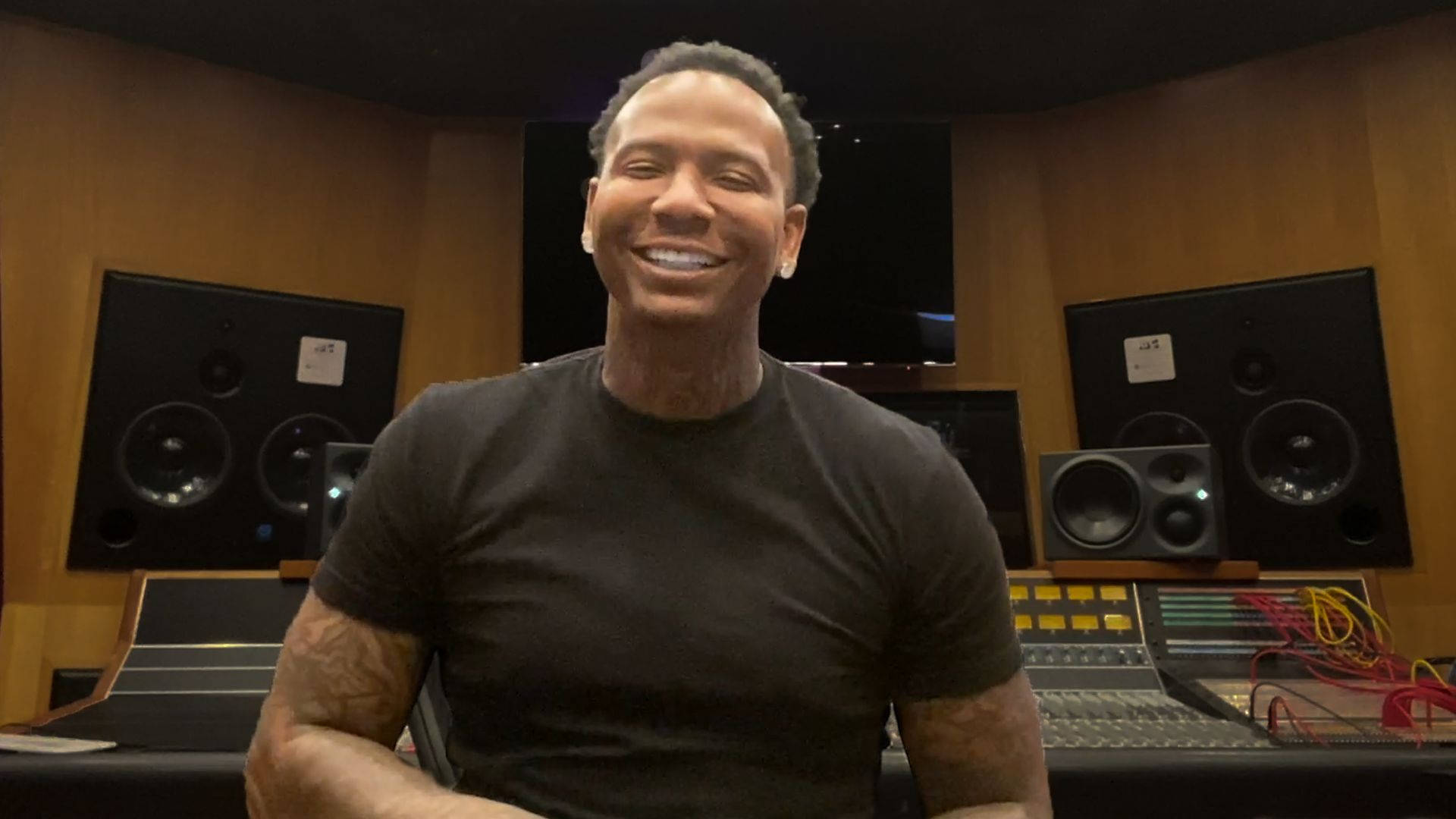 編輯版 Moneybagg Yo 壁紙 — 一位面帶微笑、有紋身的男士坐在專業錄音室裡，周圍環繞著大型揚聲器和混音控制台。