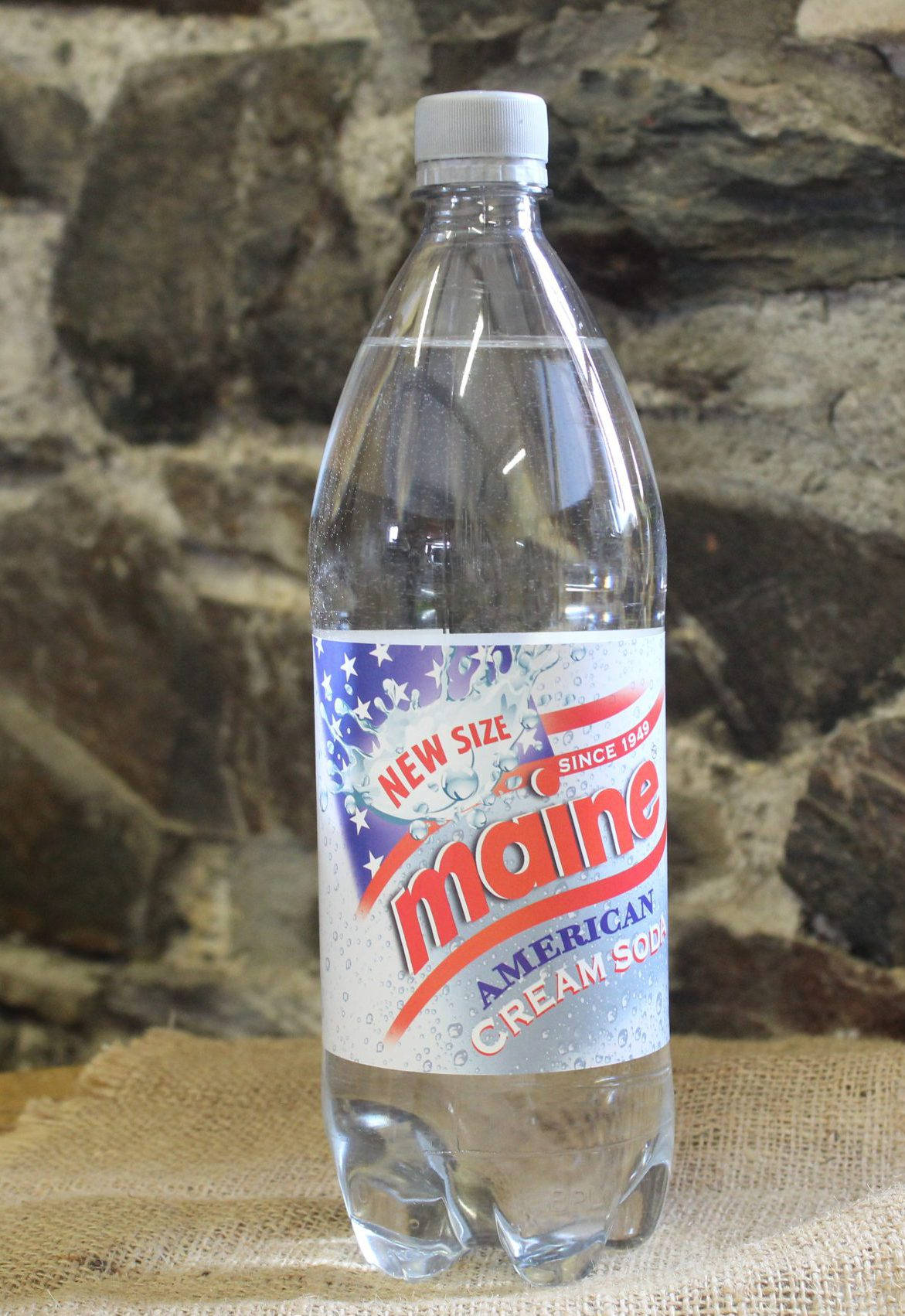 緬因美國奶油蘇打飲料瓶 壁紙 — 一瓶透明的 Maine American Cream Soda 塑膠瓶放在粗麻布上，背景是粗糙的石牆。