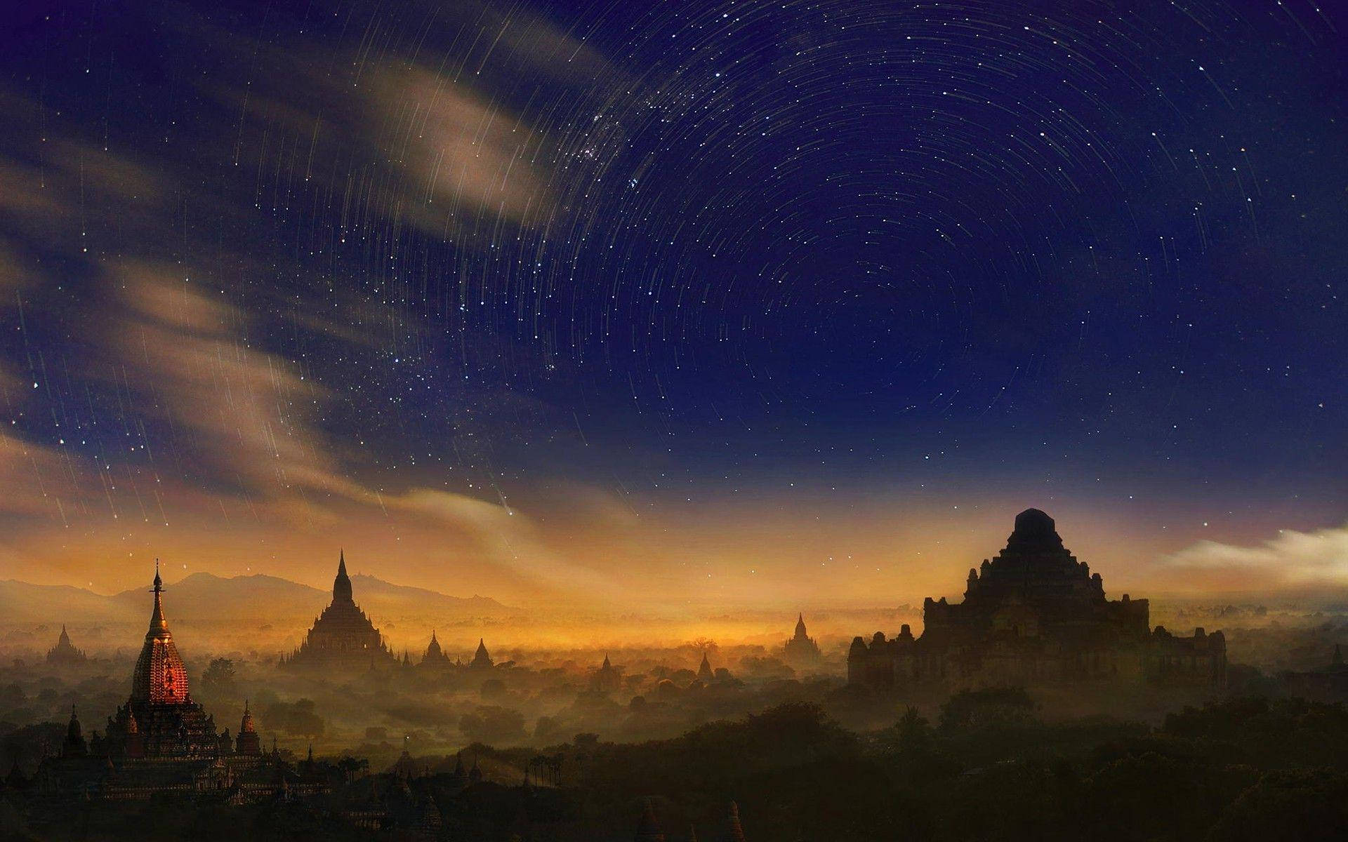 在繁星點點的夜空下，古老寶塔的剪影與可見的星軌。