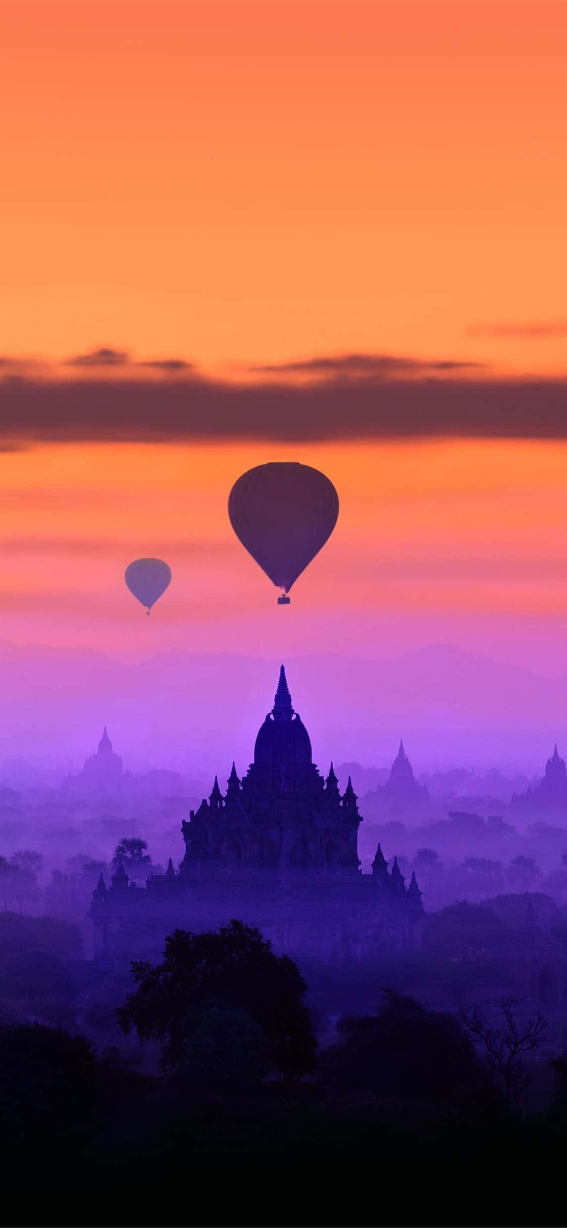熱氣球在日出時漂浮在霧濛濛的古老寺廟上方。