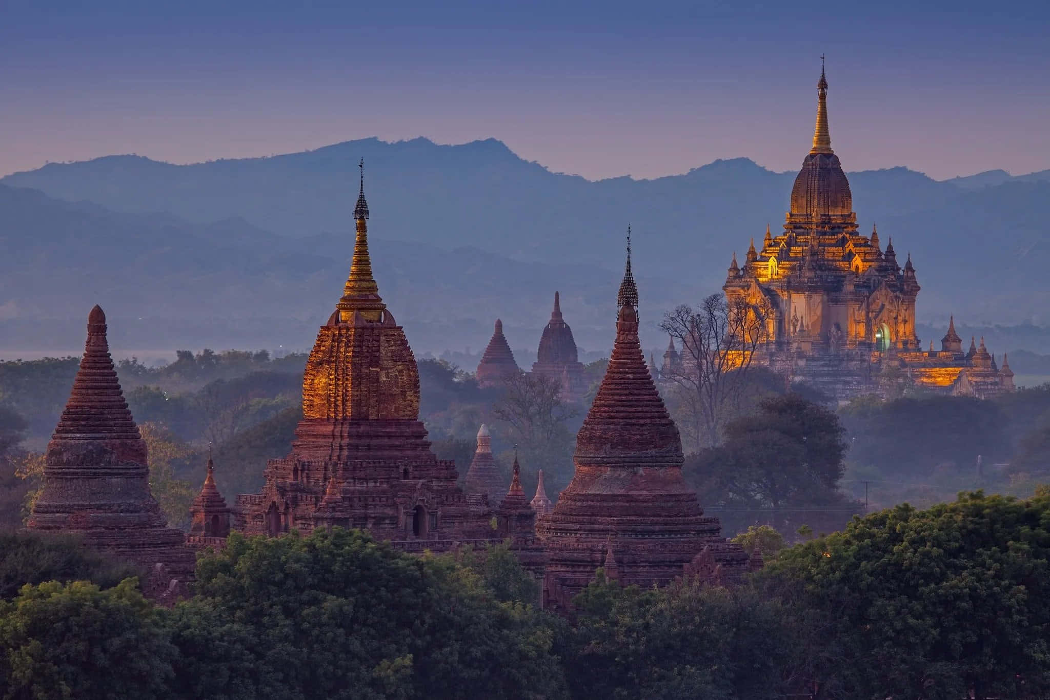 Asia 桌布 壁紙 — 緬甸黃昏時分，古老的黃金佛塔在霧氣繚繞的山巒映襯下溫暖地閃耀。