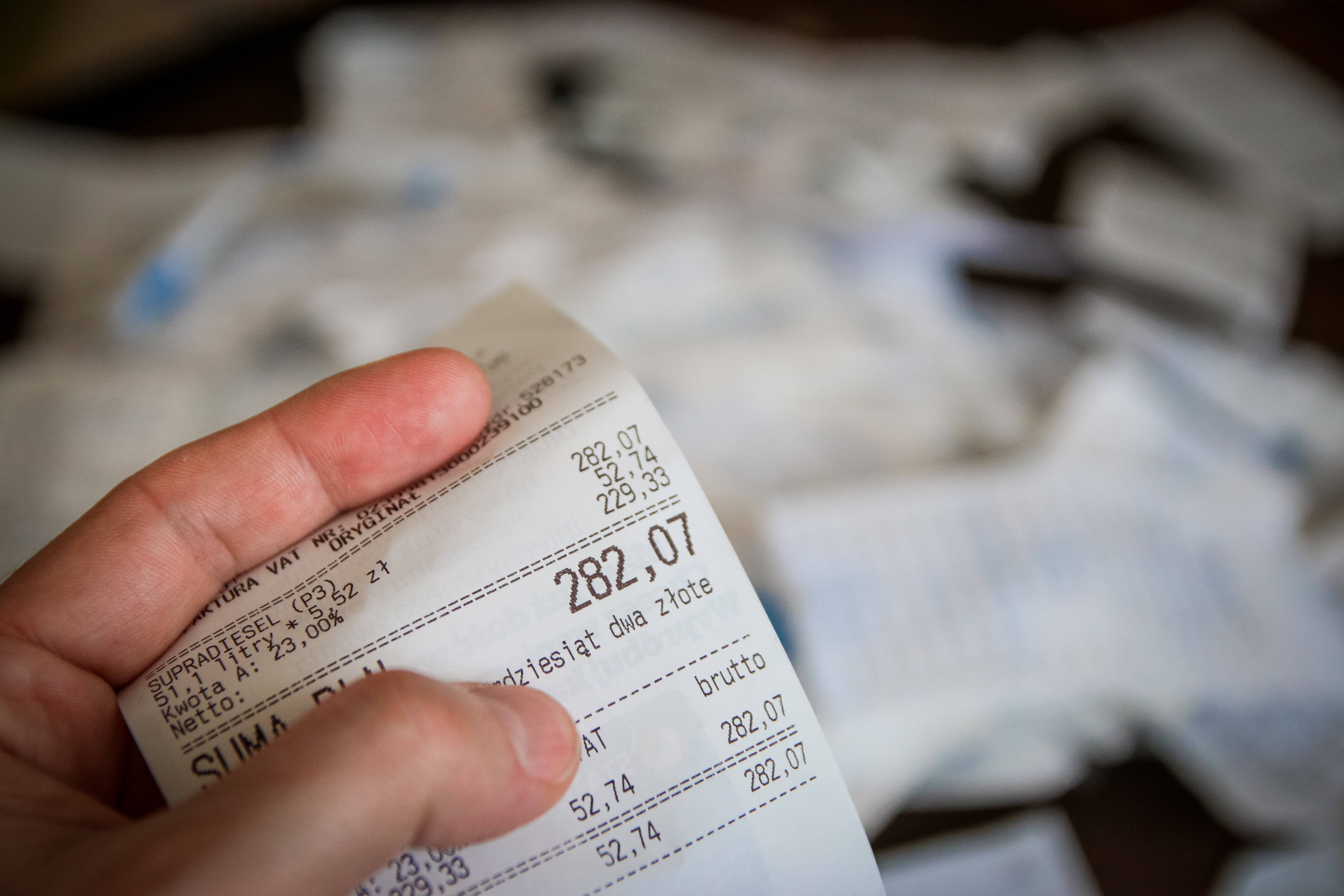 總金額282.07收據 壁紙 — 手部特寫，手持一張詳細的波蘭燃油收據，顯示總金額及增值稅明細，背景為模糊的皺紙。