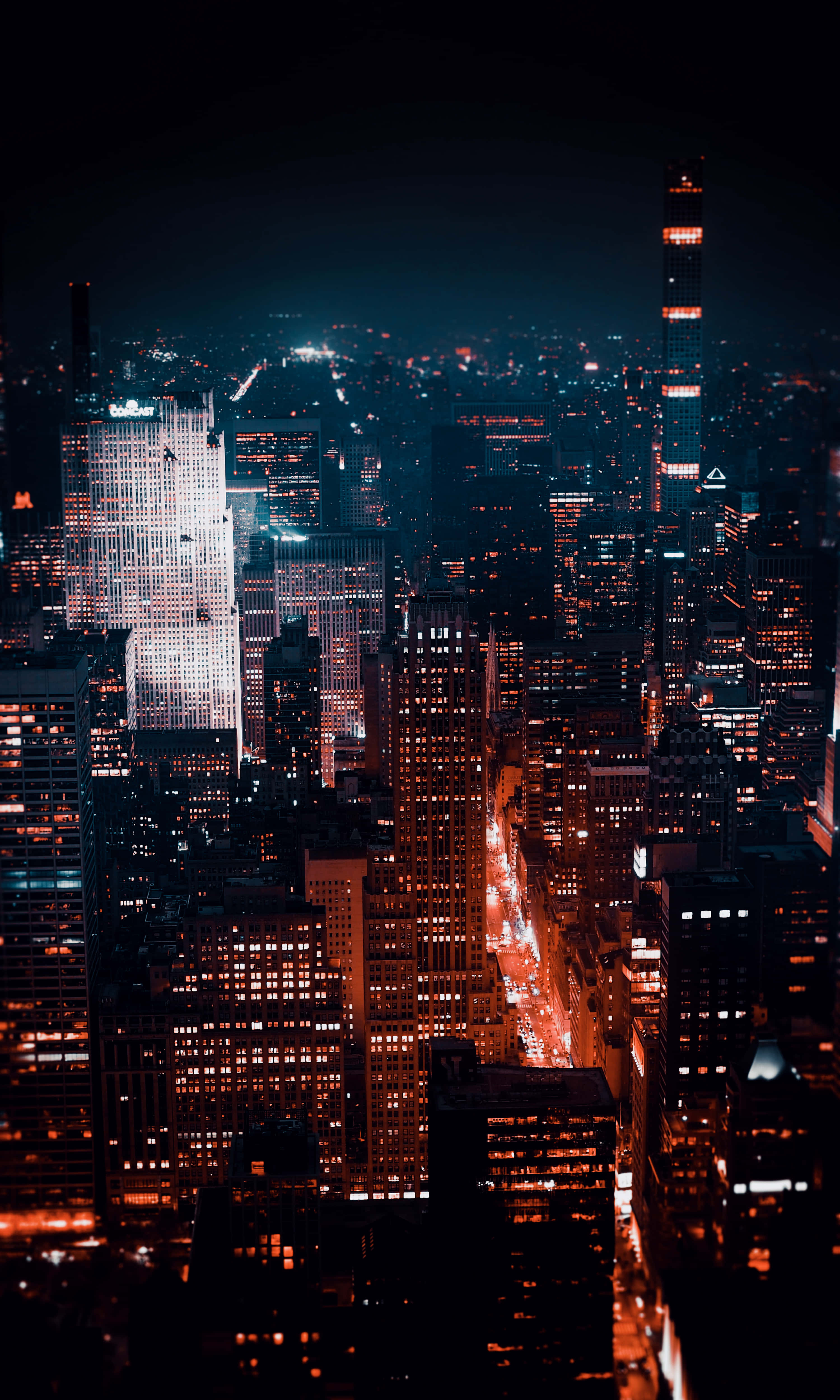 繁忙城市夜景 壁紙 — 夜晚廣闊城市的鳥瞰圖，閃爍的摩天大樓和充滿活力的橙色路燈照亮了城市峽谷。