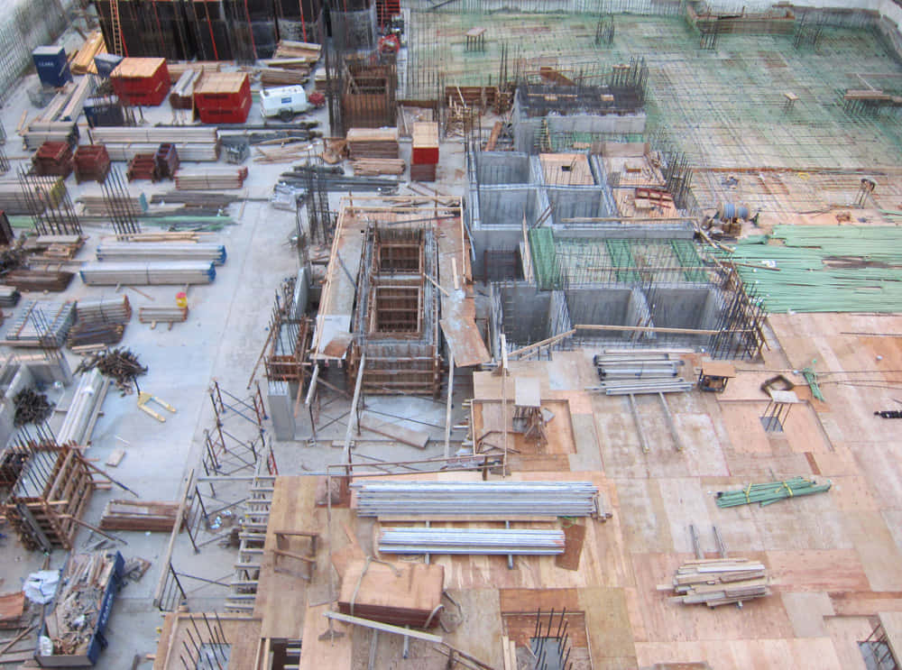 Constructivism 桌布 壁紙 — 繁忙建築工地的鳥瞰圖，有鋼筋、混凝土模板、腳手架和成堆的木材，在明亮的日光下。