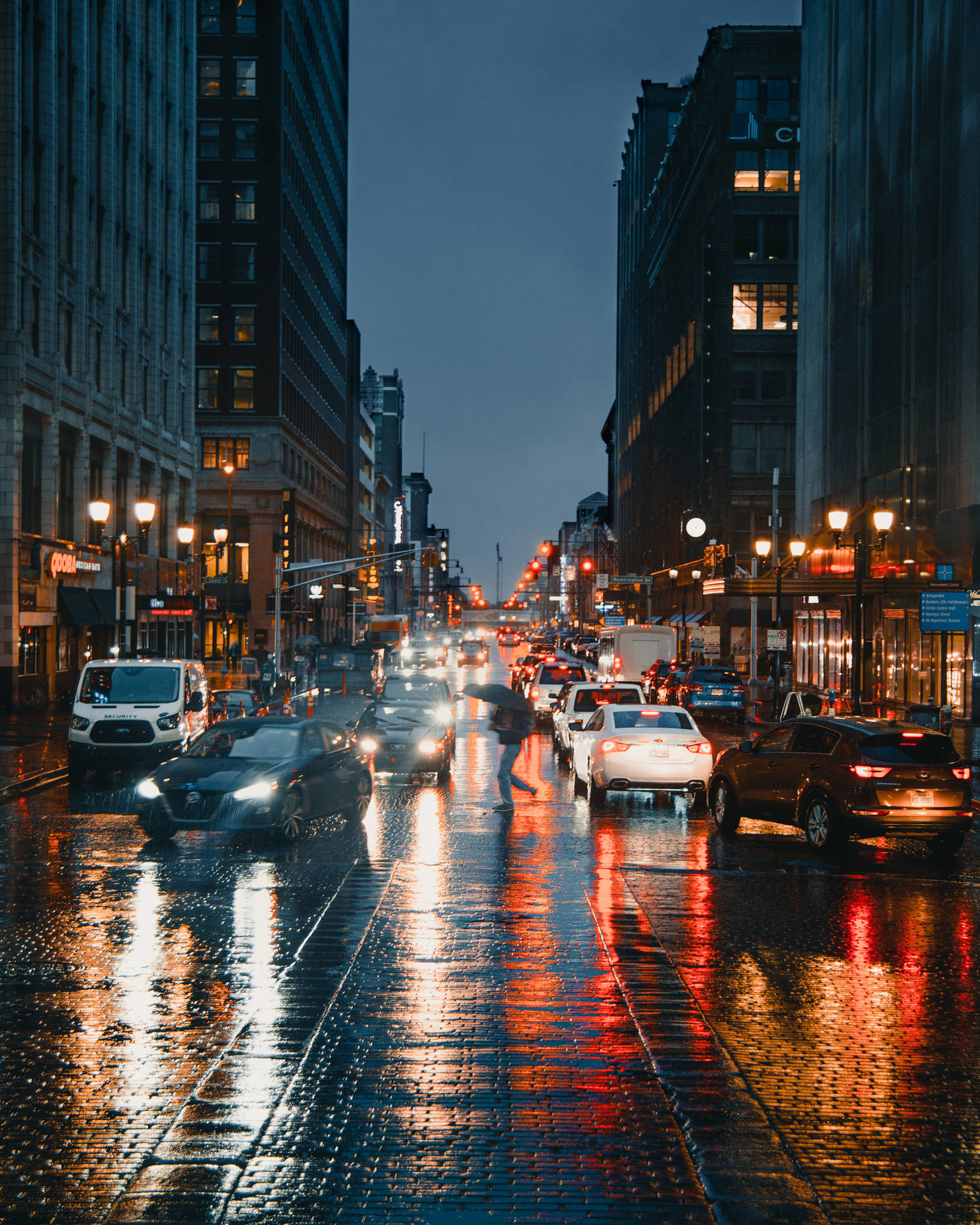 黃昏時分的城市街道，濕漉漉的鵝卵石反射著車燈和路燈。