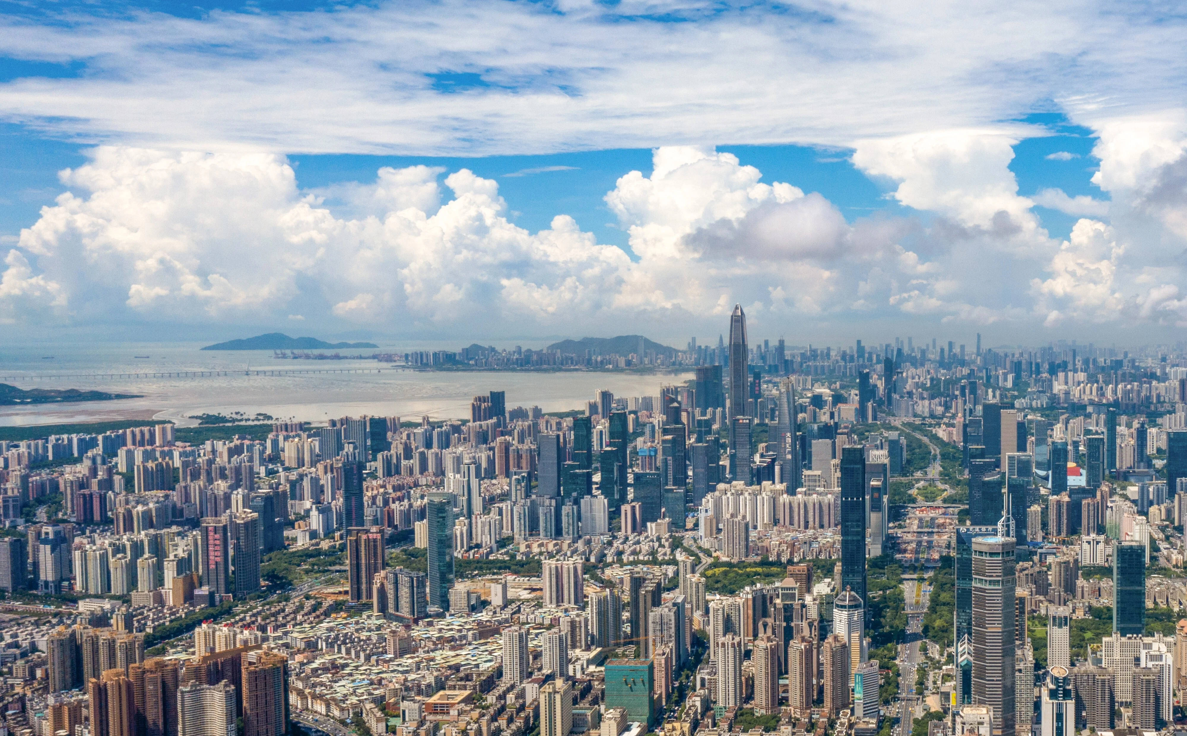 繁忙深圳城市 壁紙 — 從高空俯瞰廣闊的現代城市景觀，藍天白雲，遠處有水。