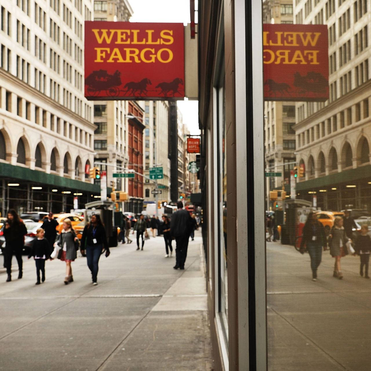 行人沿著繁忙的城市街道走過商店櫥窗中反射出的Wells Fargo標誌。