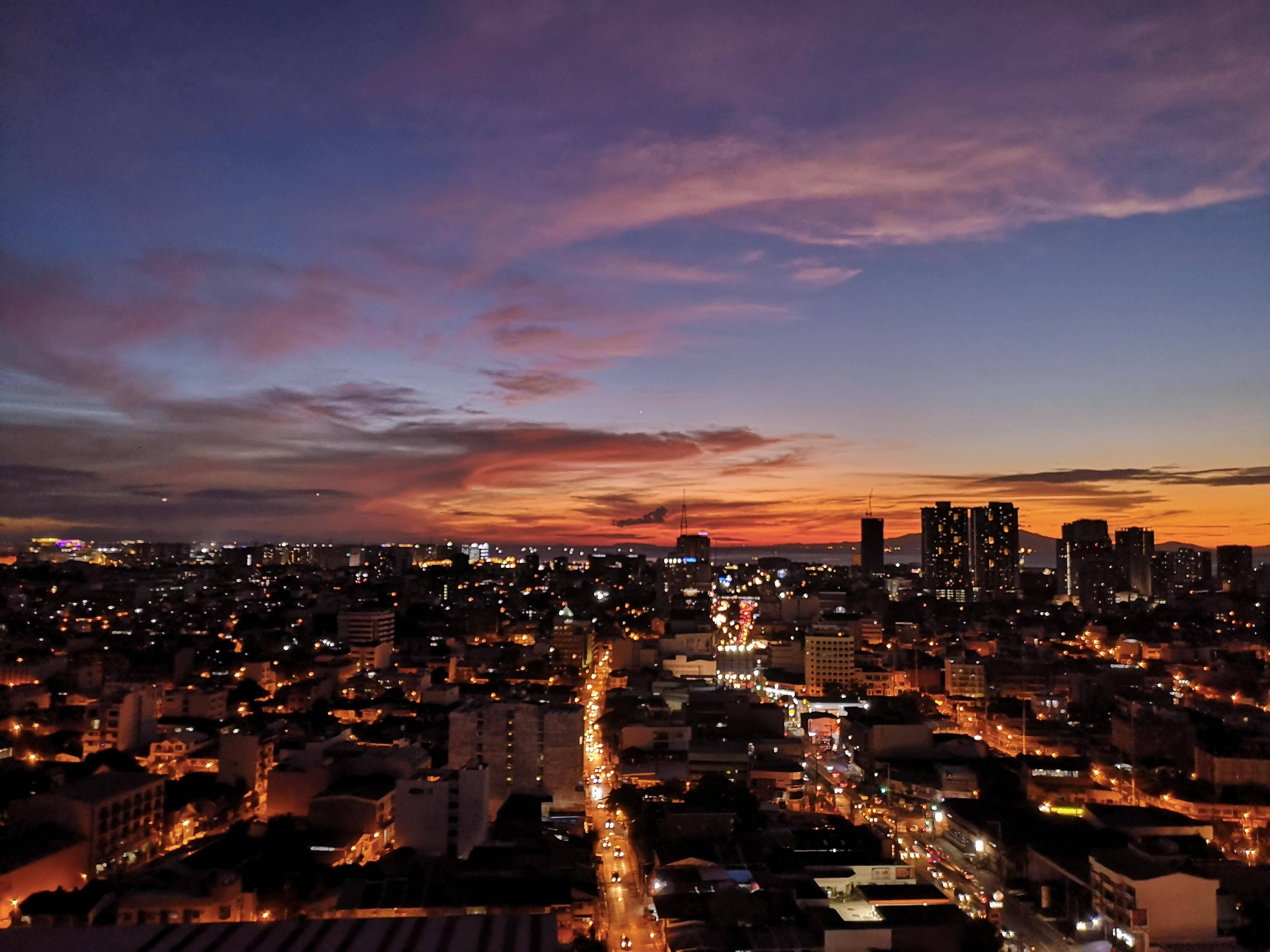 繁忙馬尼拉夜景 壁紙 — 黃昏時分充滿活力的城市景觀，在紫橙色天空下閃爍的街燈和建築物。