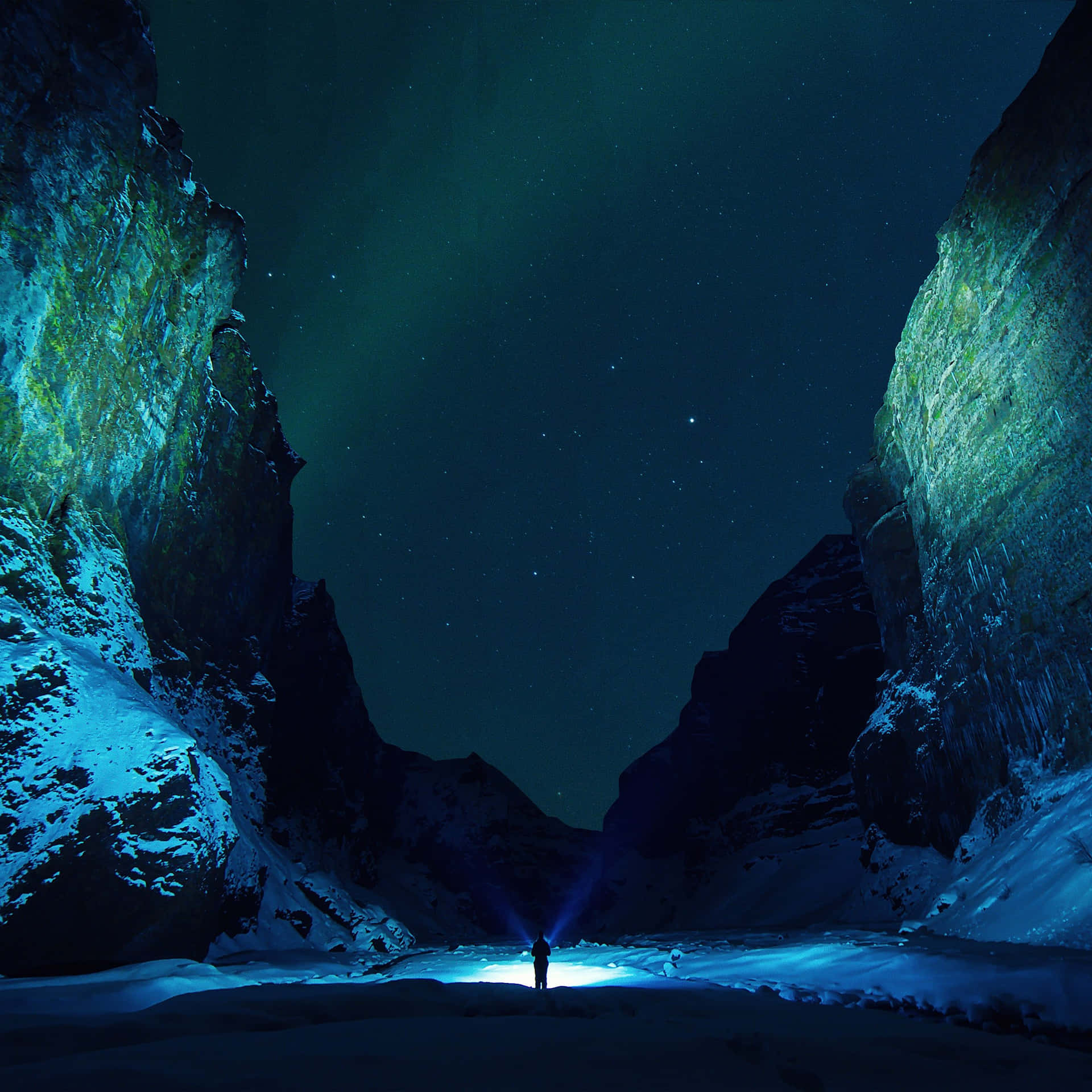 一個拿著手電筒的人在帶有極光的星空下探索積雪的峽谷。