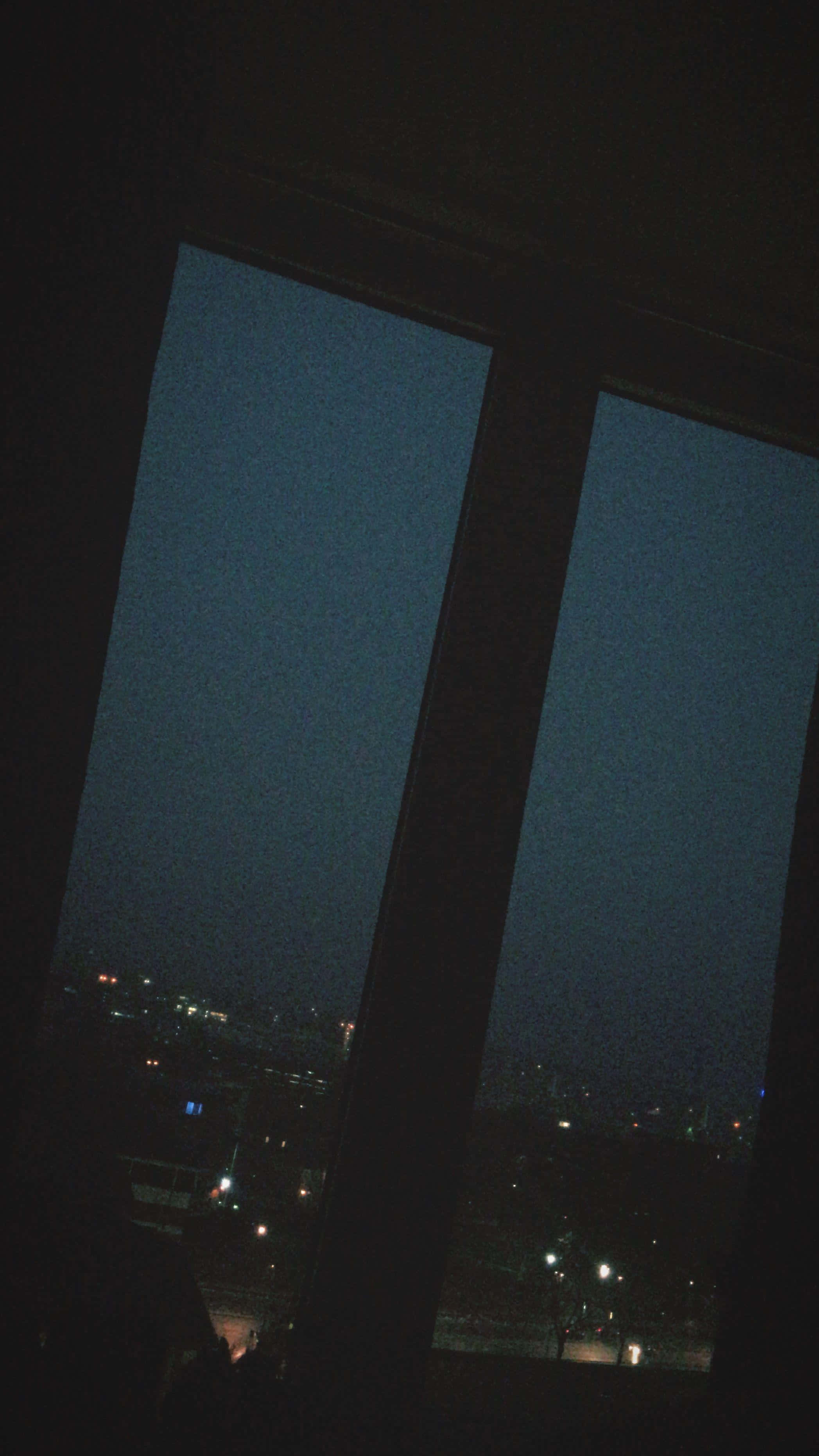 繁星夜空的美麗 壁紙 — 一個昏暗的窗框捕捉到在深邃暮色天空下，散落燈光閃爍的城市景觀。