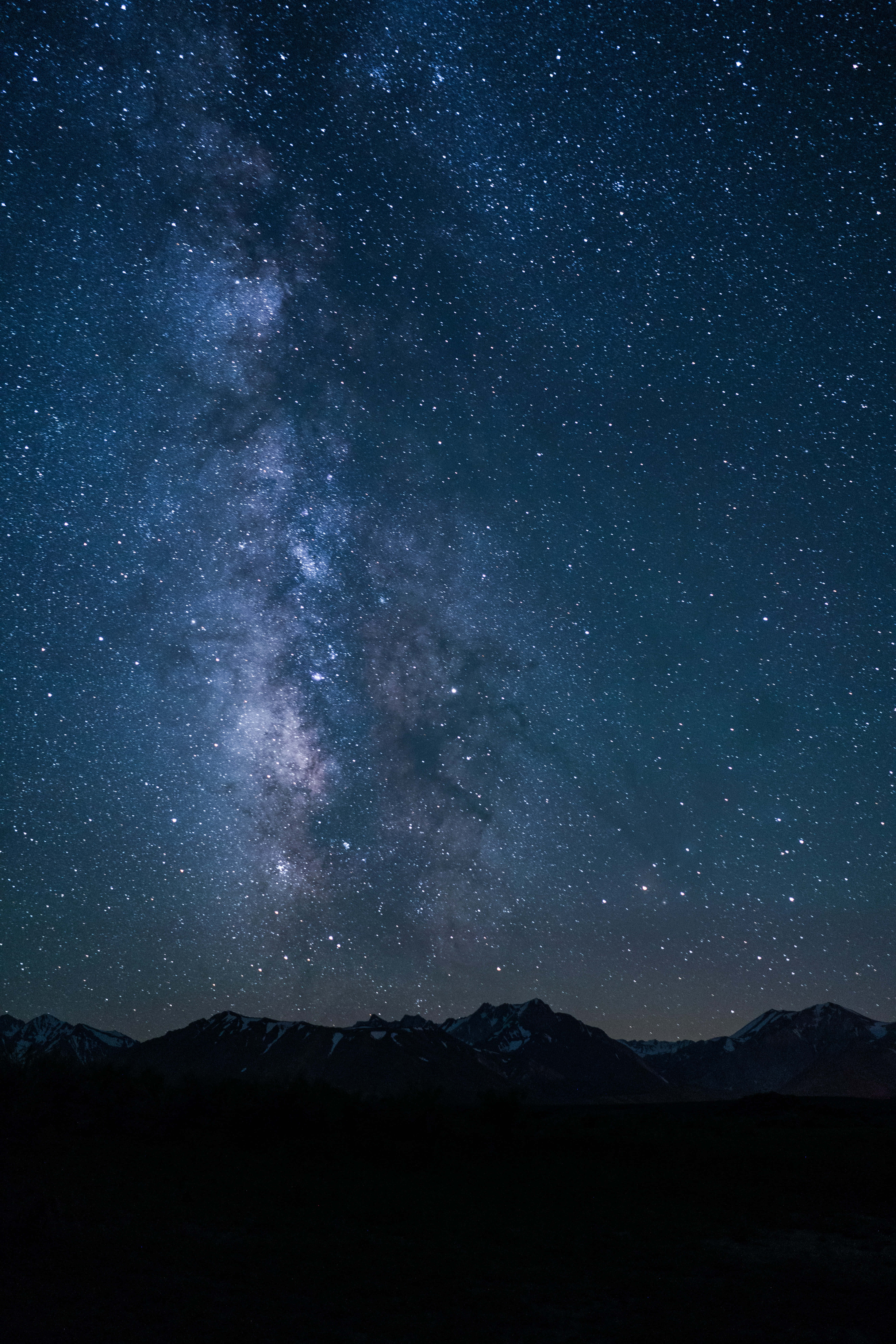 繁星夜空的難以置信之美 壁紙 — 一個令人屏息的夜空，充滿無數星星和銀河，在黑暗的山脈輪廓上拱起。