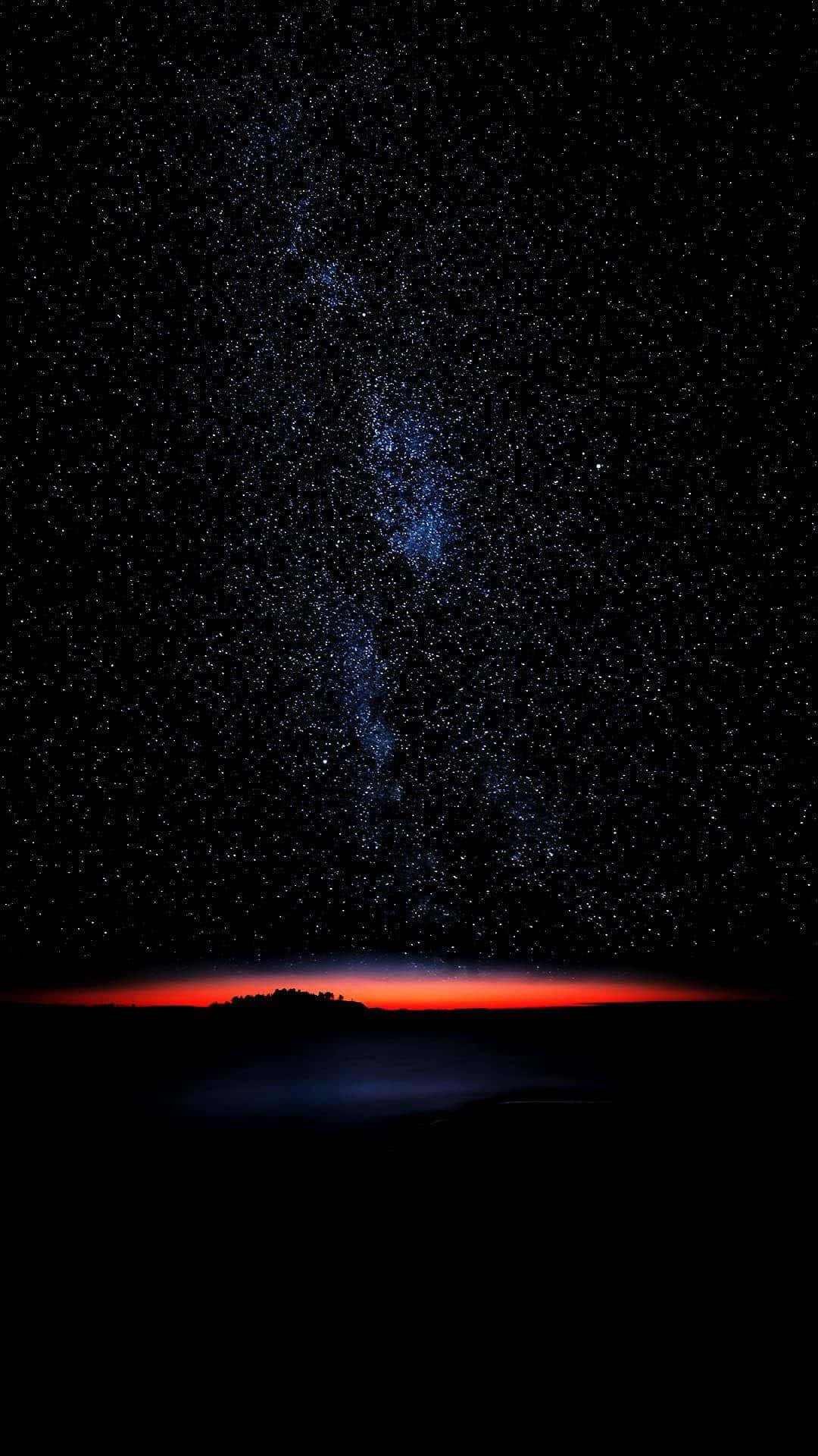 繁星夜空超 AMOLED 顯示器 壁紙 — 一個令人嘆為觀止的夜空，充滿了無數的星星，一條發光的藍色銀河在黑暗的地平線上拱起，被鮮紅色的光芒照亮。