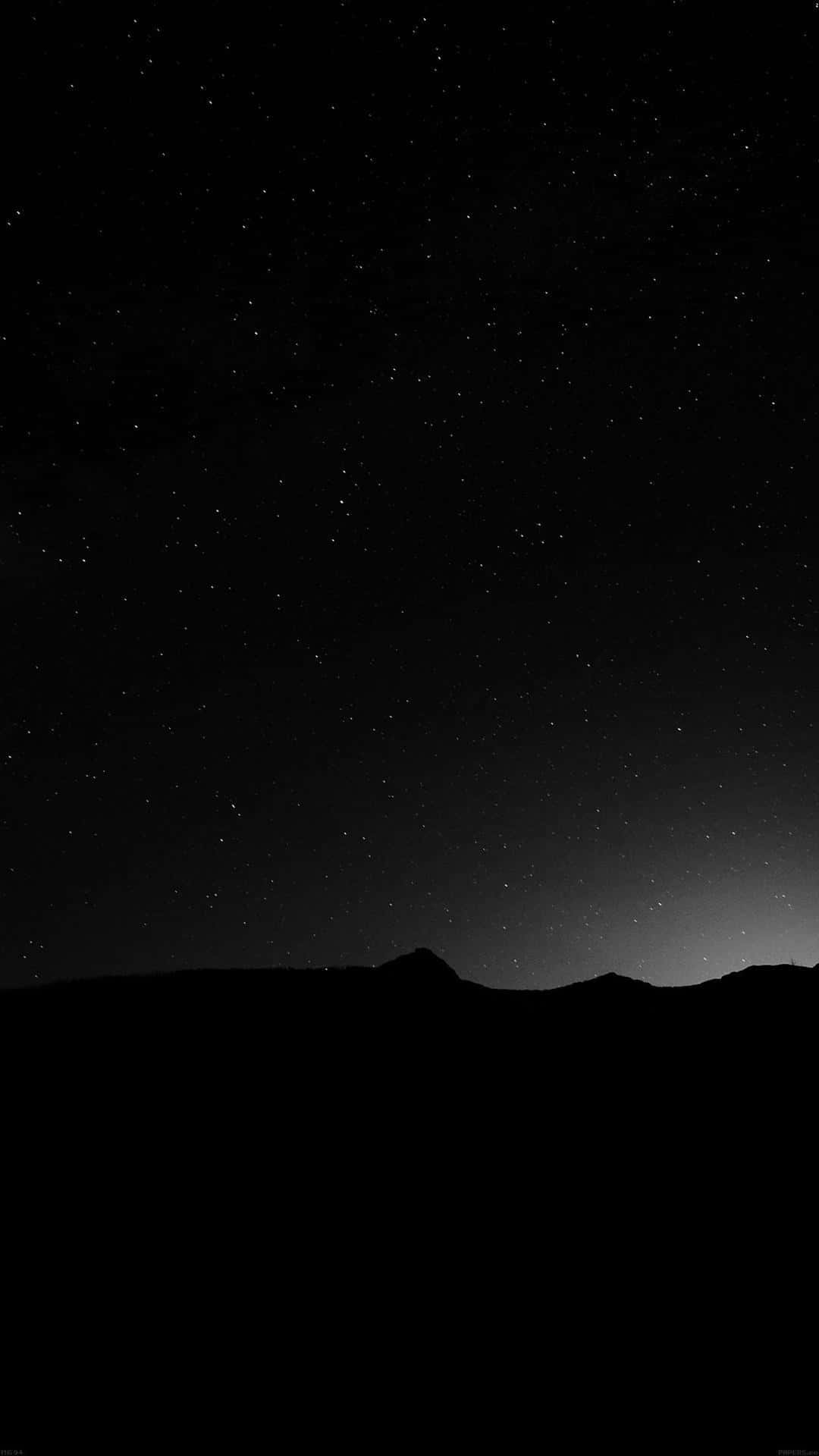 黑暗的山脈輪廓在繁星點點的夜空下，地平線上有微弱的光芒。