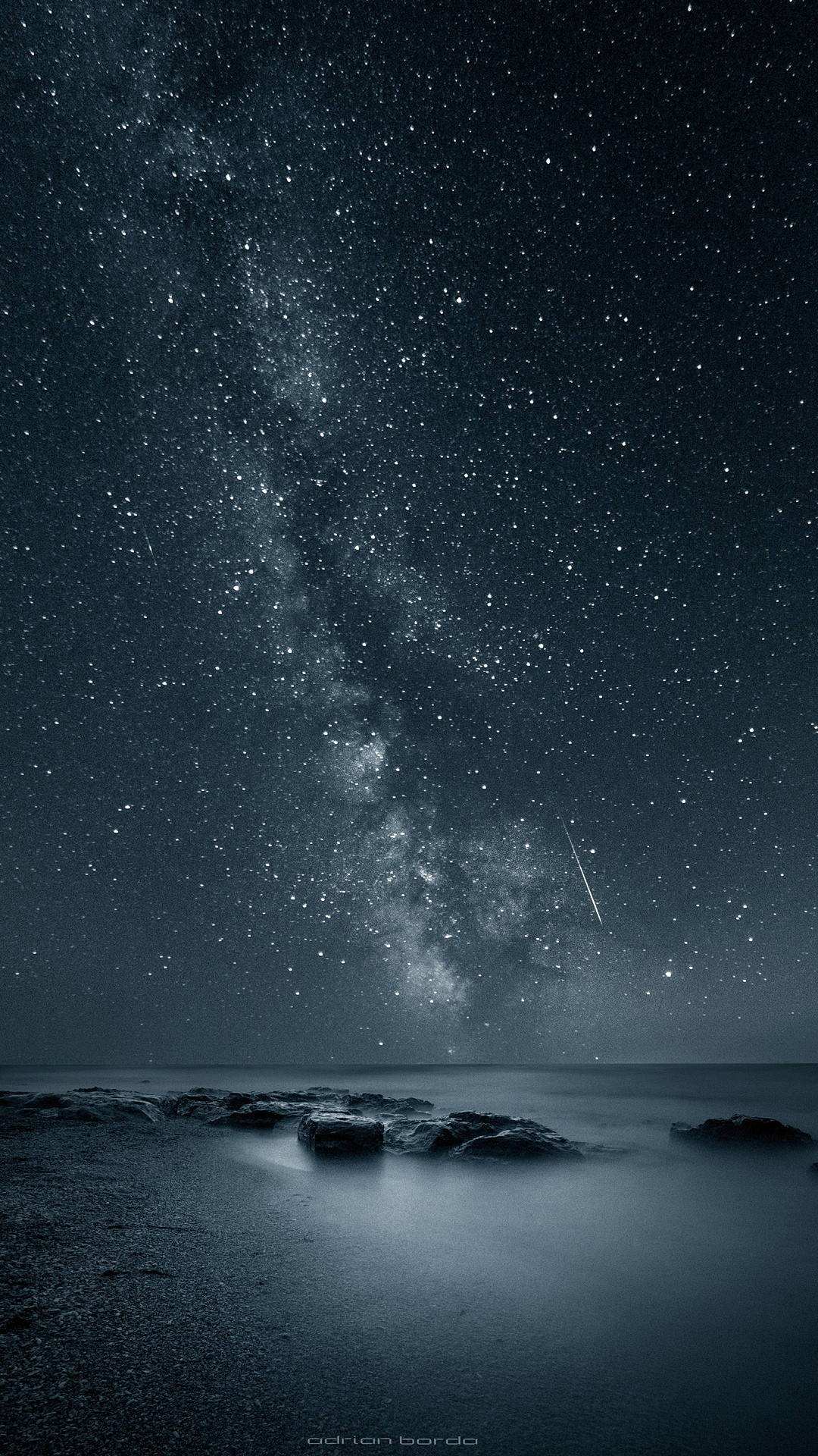繁星滿天 iPhone 8 動態背景 壁紙 — 繁星點點的夜空，銀河與流星在平靜的海洋和前景的深色岩石上方拱起。