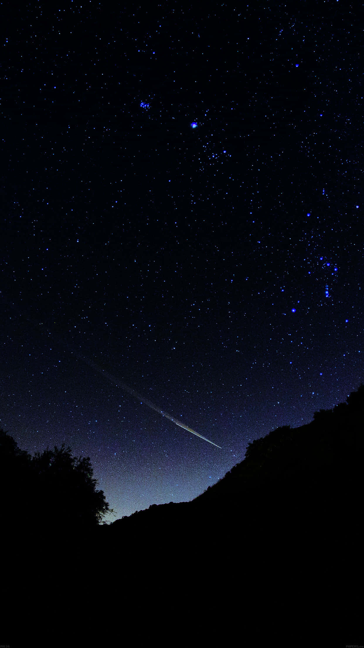繁星滿天的夜空 壁紙 — 一顆明亮的流星劃過繁星點點的夜空，下方是黑暗的山丘和樹木剪影。