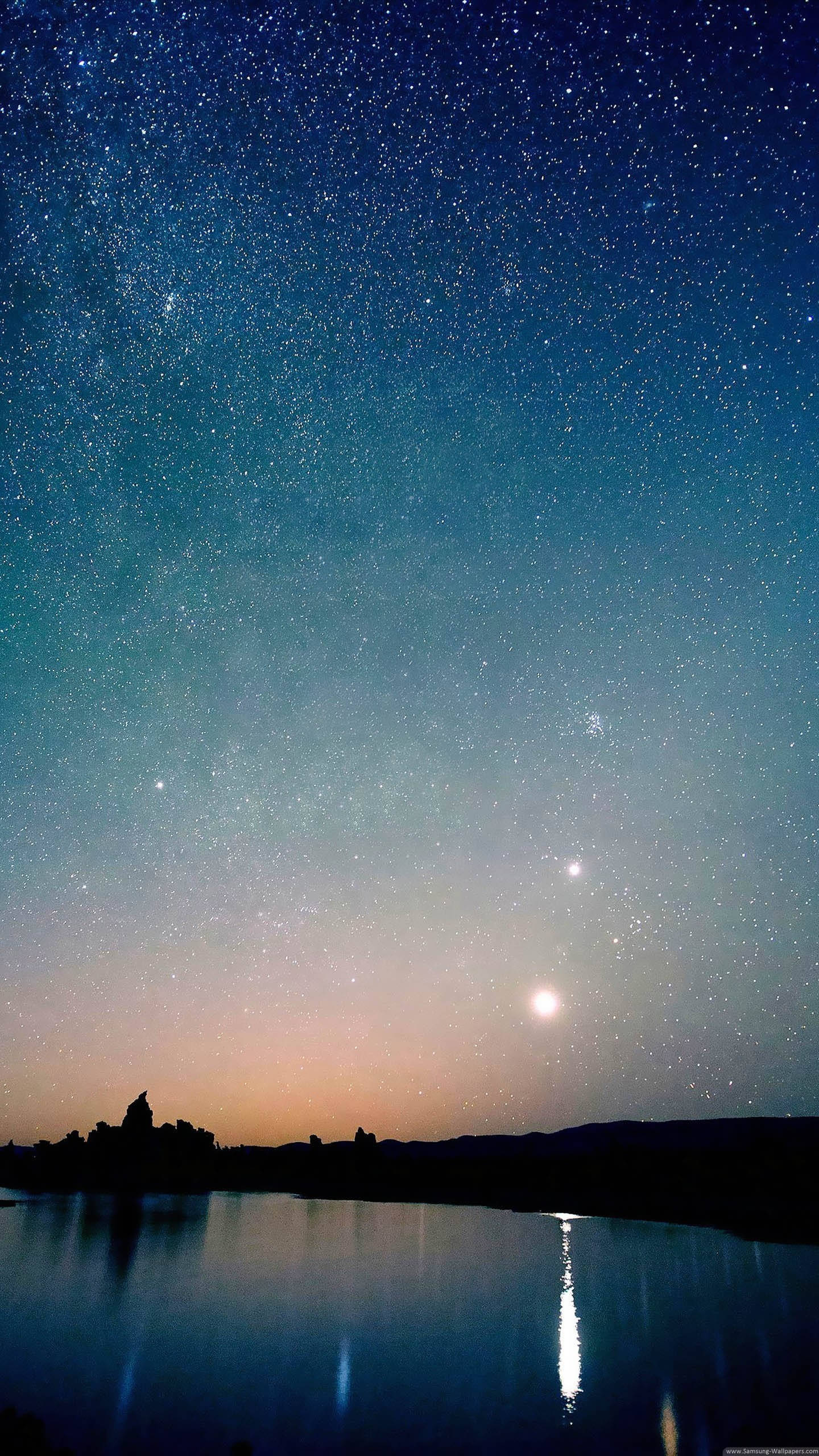 繁星點綴的美麗夜空 壁紙 — 星空之夜，明亮的月亮和星星倒映在平靜的湖面上，下方是剪影般的山丘。
