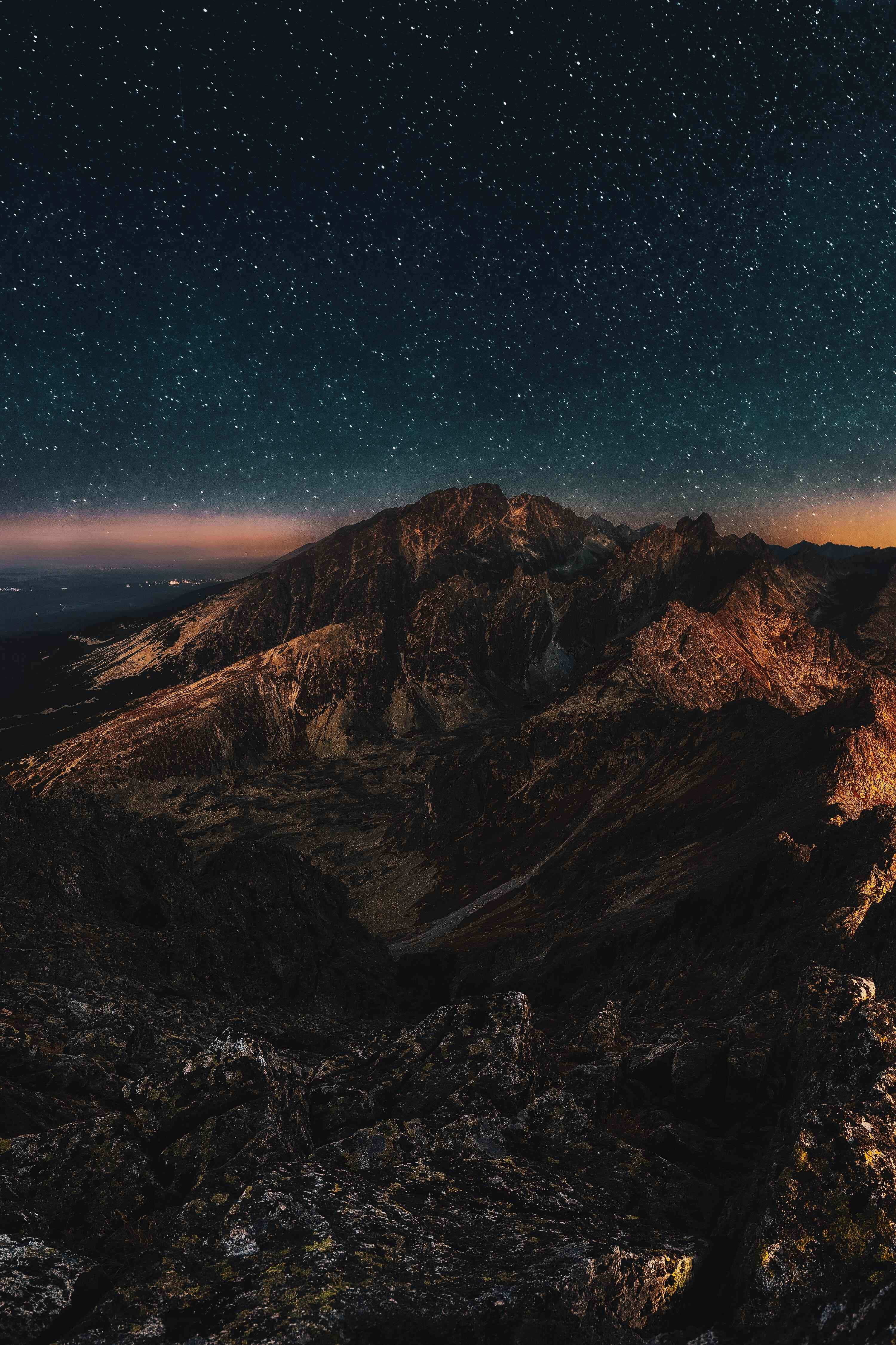 Retina Display 桌布 壁紙 — 繁星點點的夜空在鋸齒狀的山峰上方閃耀，溫暖的橙色光芒照亮了岩石地形。