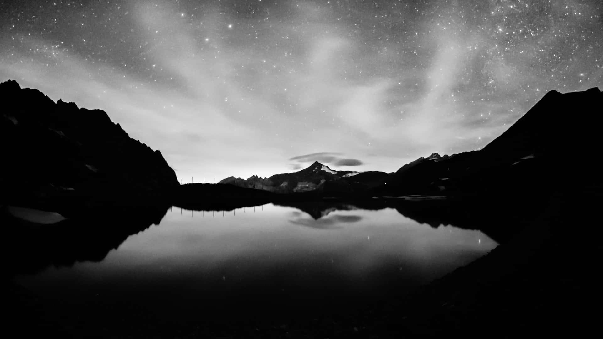 深色模式 桌布 壁紙 — 繁星點點的夜空完美地倒映在平靜的山間湖面上，四周環繞著黑暗的山峰剪影。