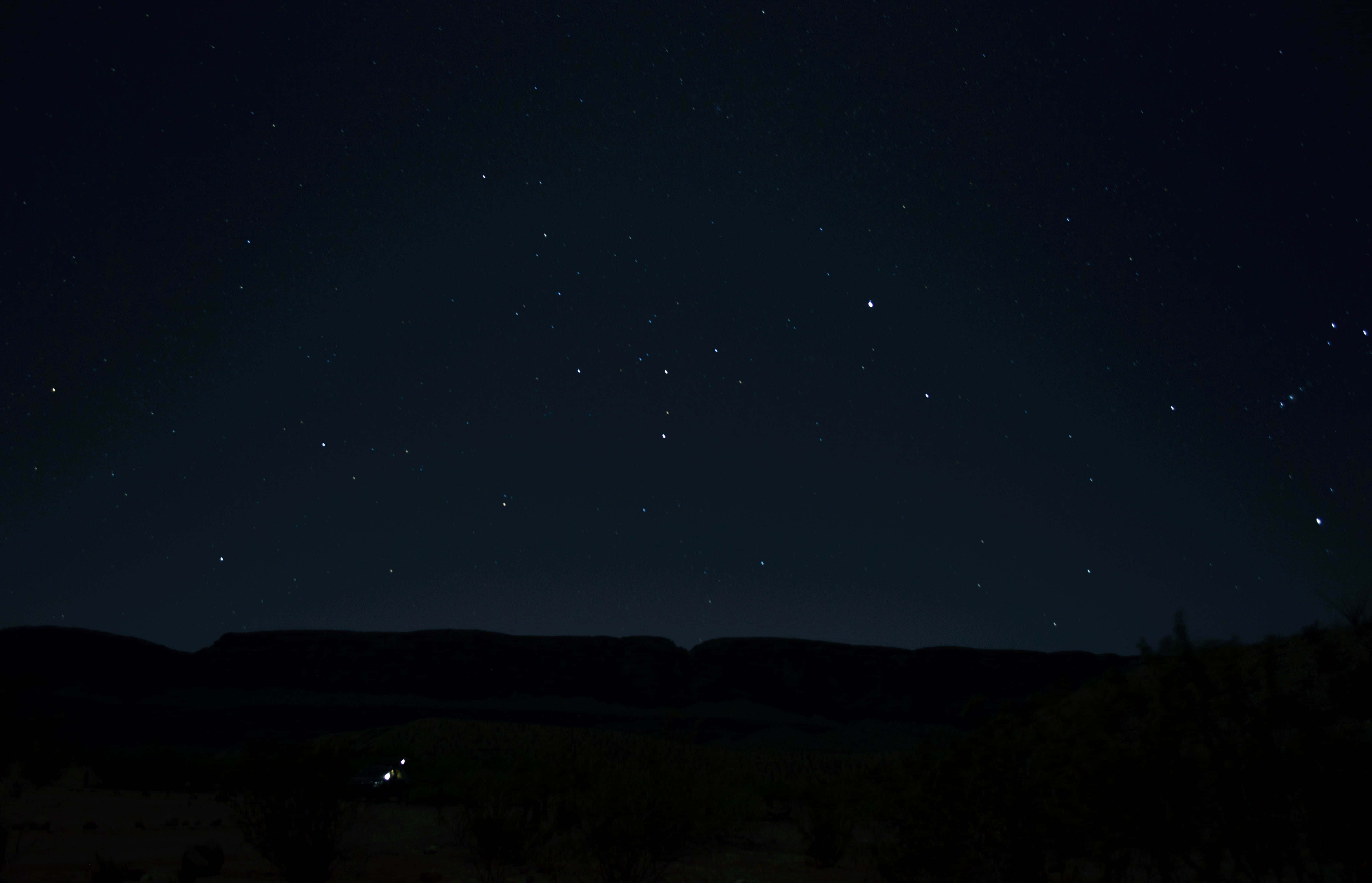 Dark Sky 桌布 壁紙 — 繁星點點的夜空拱起在深靛藍色天空下，黑暗剪影的沙漠台地和稀疏植被之上。