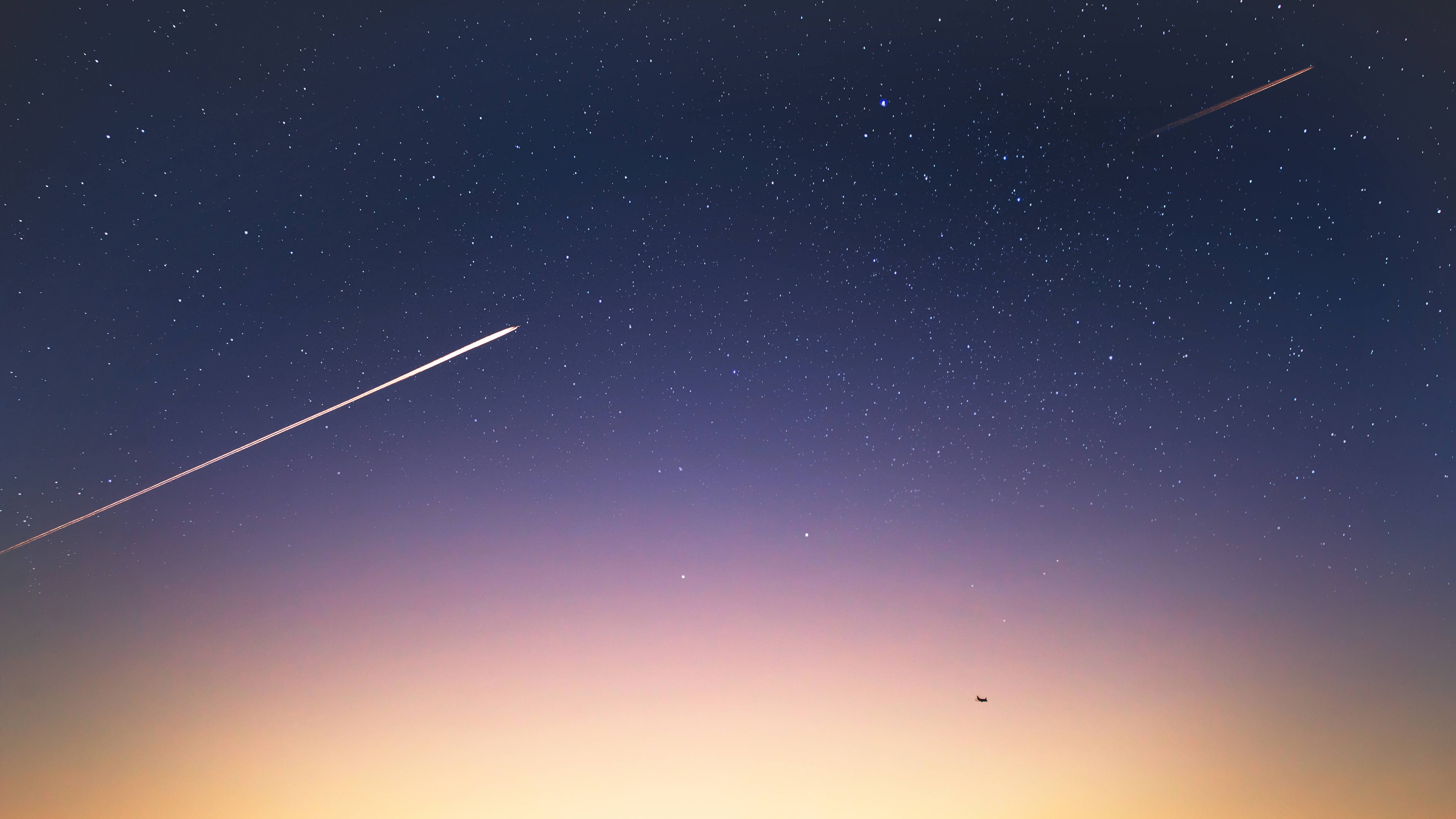Shooting Star 桌布 壁紙 — 繁星點點的暮色天空，有兩條明亮的飛機尾跡和遠處的剪影，背景是從深藍色到暖橙色的漸變。