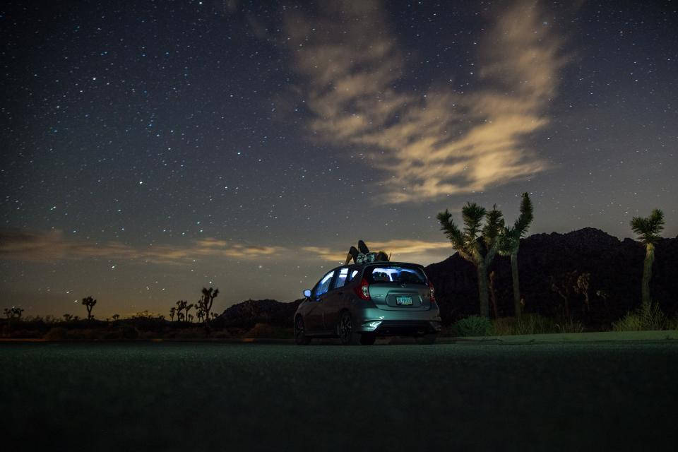 繁星點點的美麗夜景 壁紙 — 一輛銀色汽車停泊在繁星點點的沙漠夜空下，車頂上坐著兩個人，附近有約書亞樹。