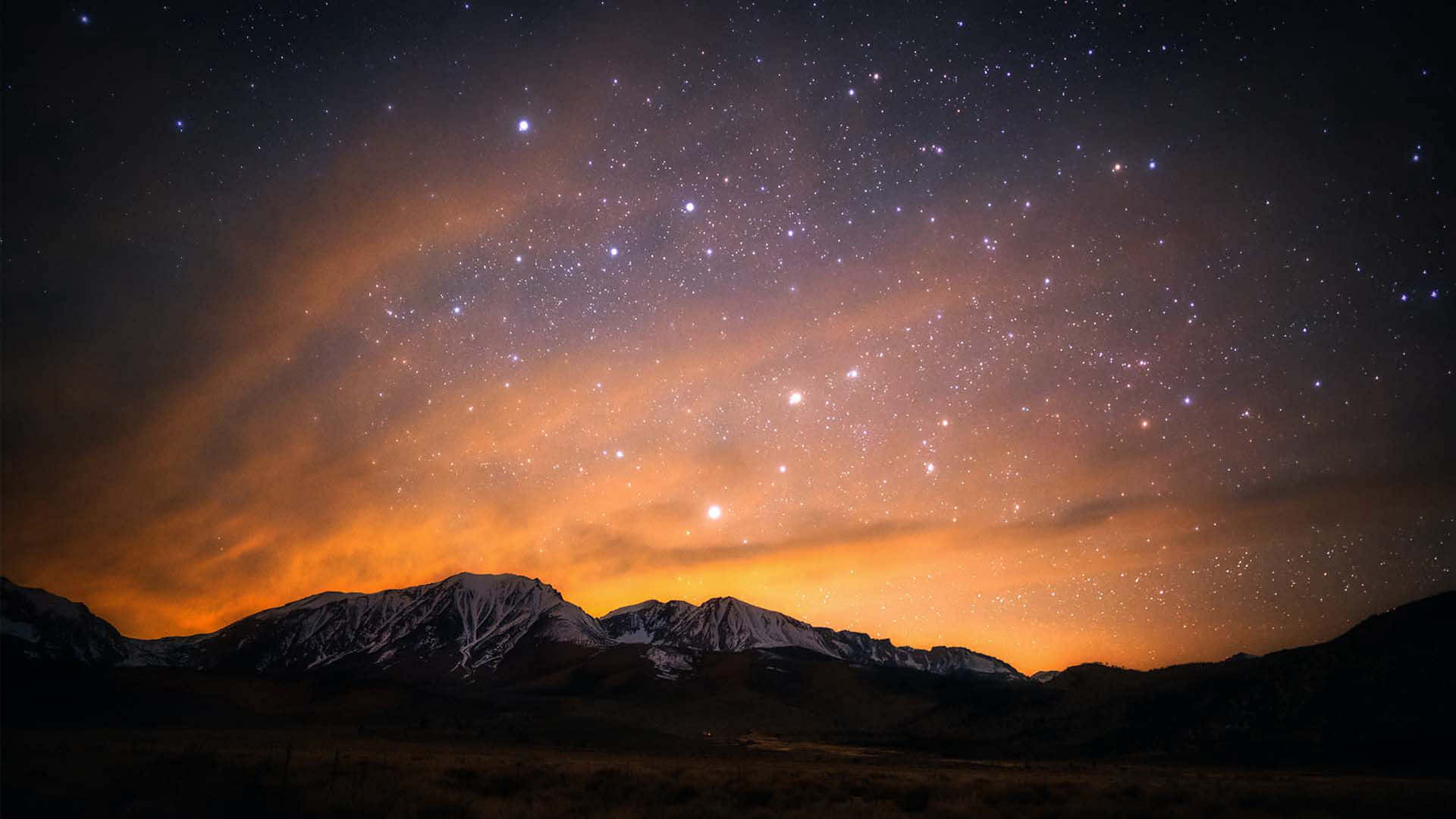 繁星點點的美麗夜空 壁紙 — 積雪的山峰剪影，在充滿活力的星空夜空下，閃耀著橙色極光雲。