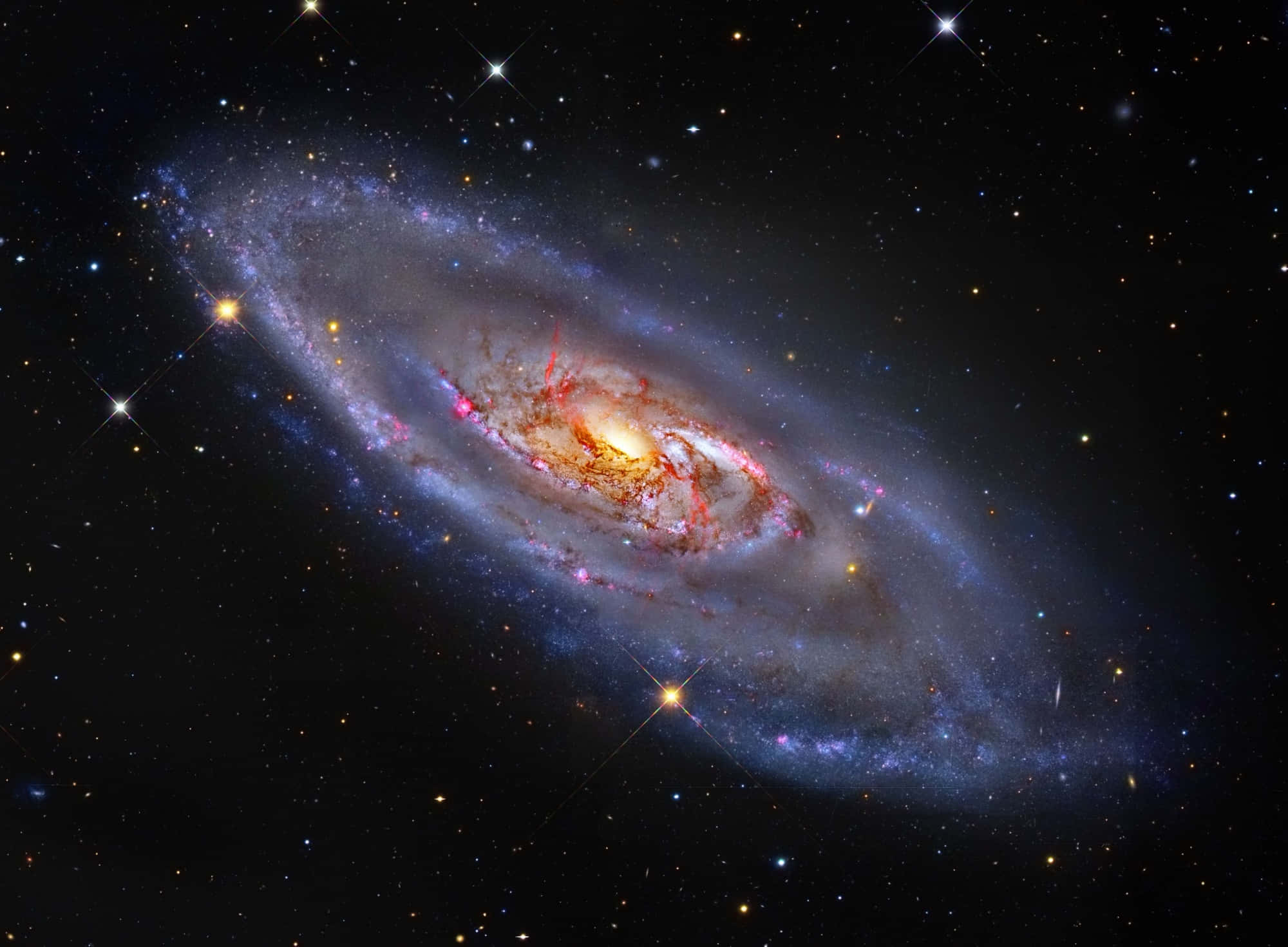 繁星點點的銀河，於深邃夜空熠熠生輝 壁紙 — 一個令人驚嘆的螺旋星系，帶有發光的橙色核心和藍紫色旋臂，在星場中旋轉。