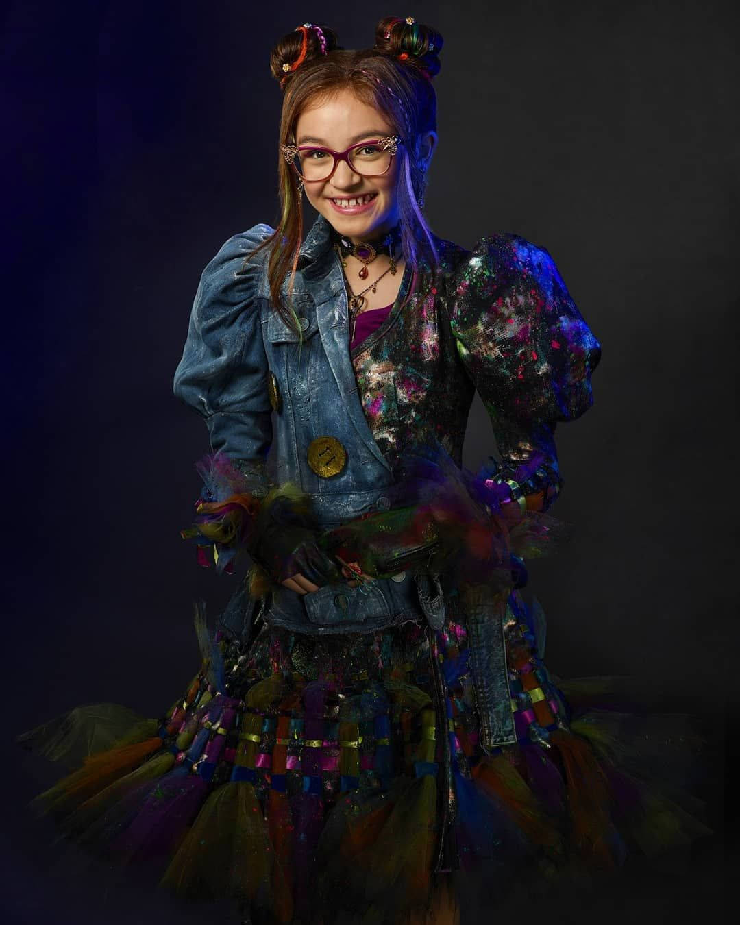 一位微笑的女孩，穿著色彩繽紛的龐克風格服裝，戴著眼鏡和羽毛裙。