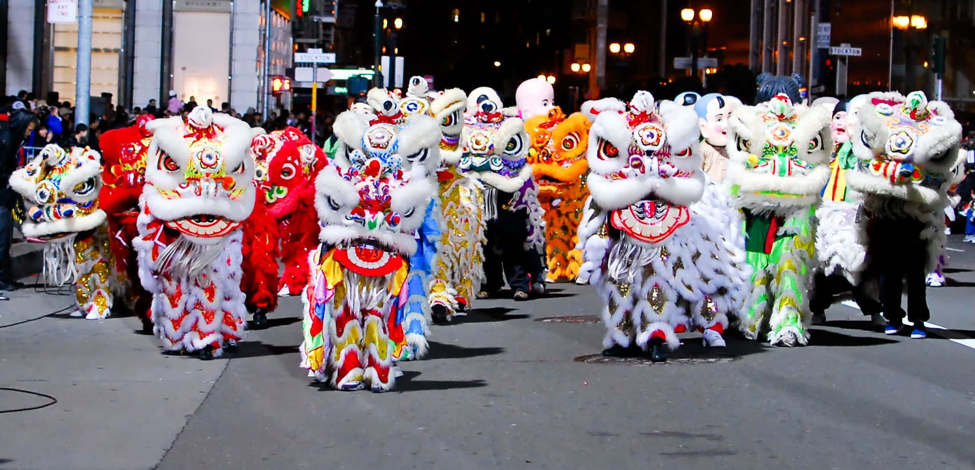 繽紛喜慶的中國新年慶祝活動 壁紙 — 色彩繽紛的舞獅表演者穿著鮮豔服裝，在夜晚的路燈下沿著城市街道遊行。