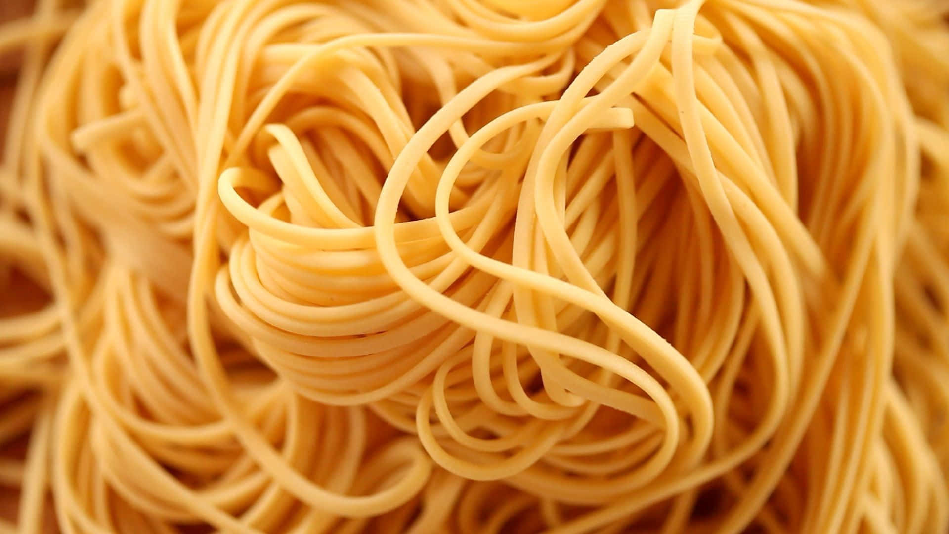 Noodles 桌布 壁紙 — 纏繞的金黃色意大利麵條的特寫，背景柔和模糊。