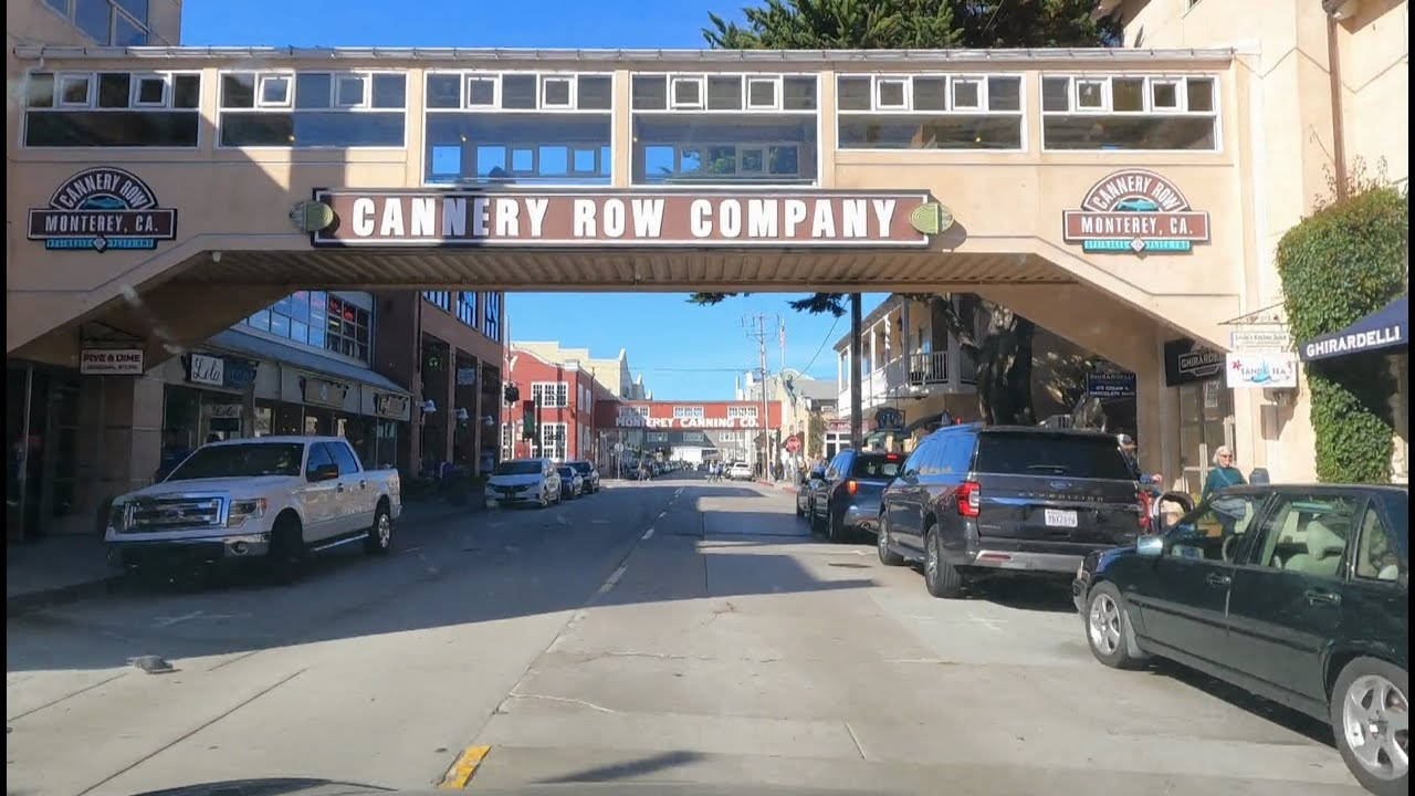 罐頭廠街建築招牌 壁紙 — 在Cannery Row Company行人天橋下的陽光街景，路邊停有汽車和商店門面。