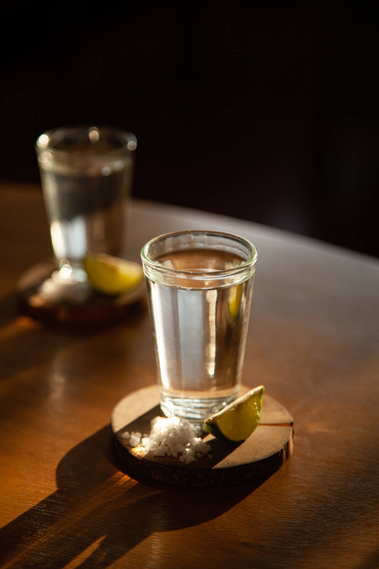 兩杯龍舌蘭酒配上鹽和青檸，放在木杯墊上，置於深色木桌上。
