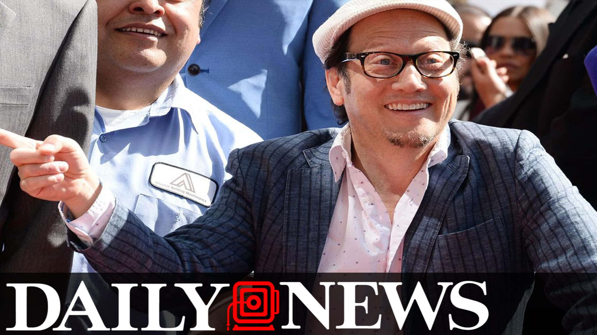 穿西裝戴帽子的男士在公共活動中微笑並指向前方。